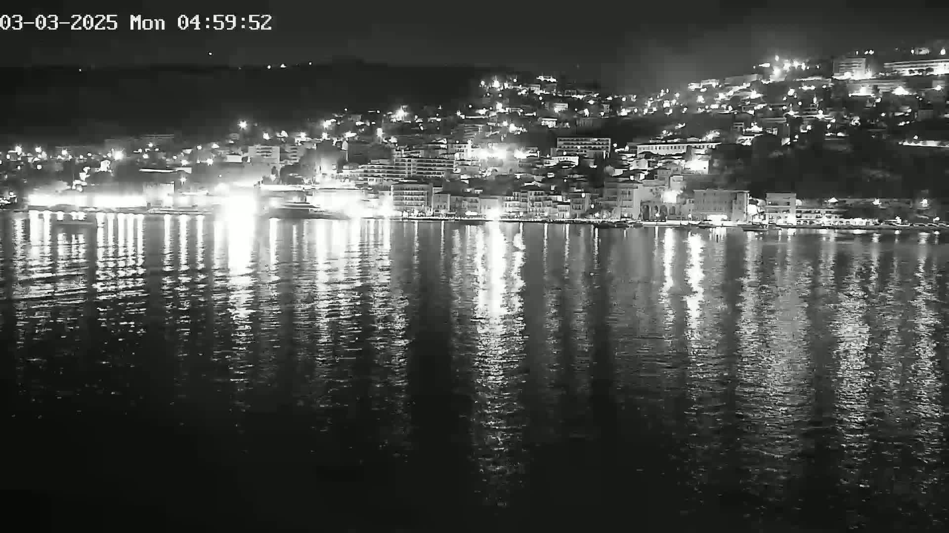 A brightly lit city at night is reflected in the dark water of a calm bay.