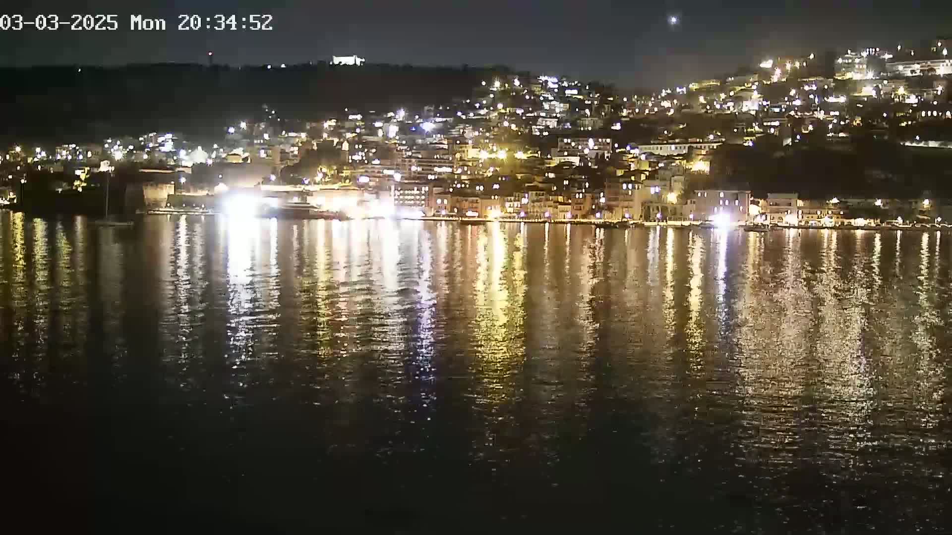 A nighttime view of a waterfront town with its lights reflected in calm water.