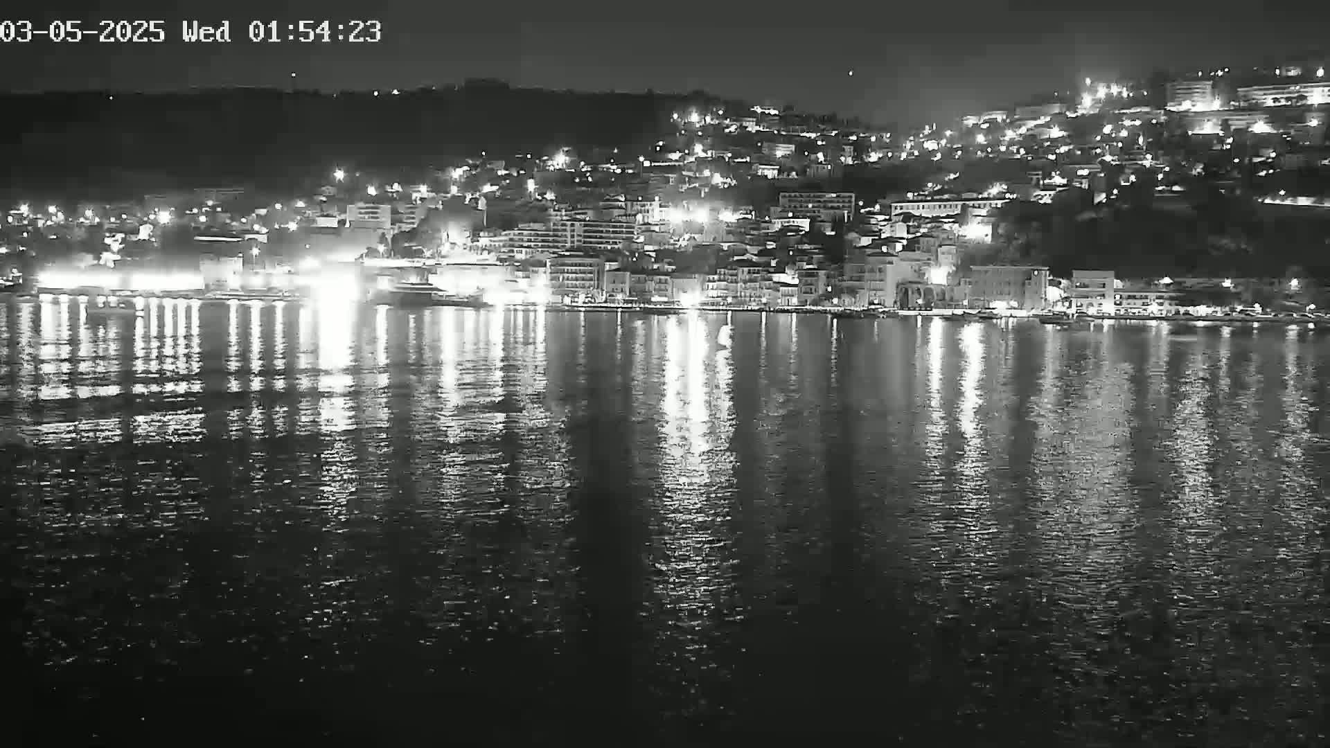 A nighttime view of a city's waterfront, illuminated by lights reflected on calm water.