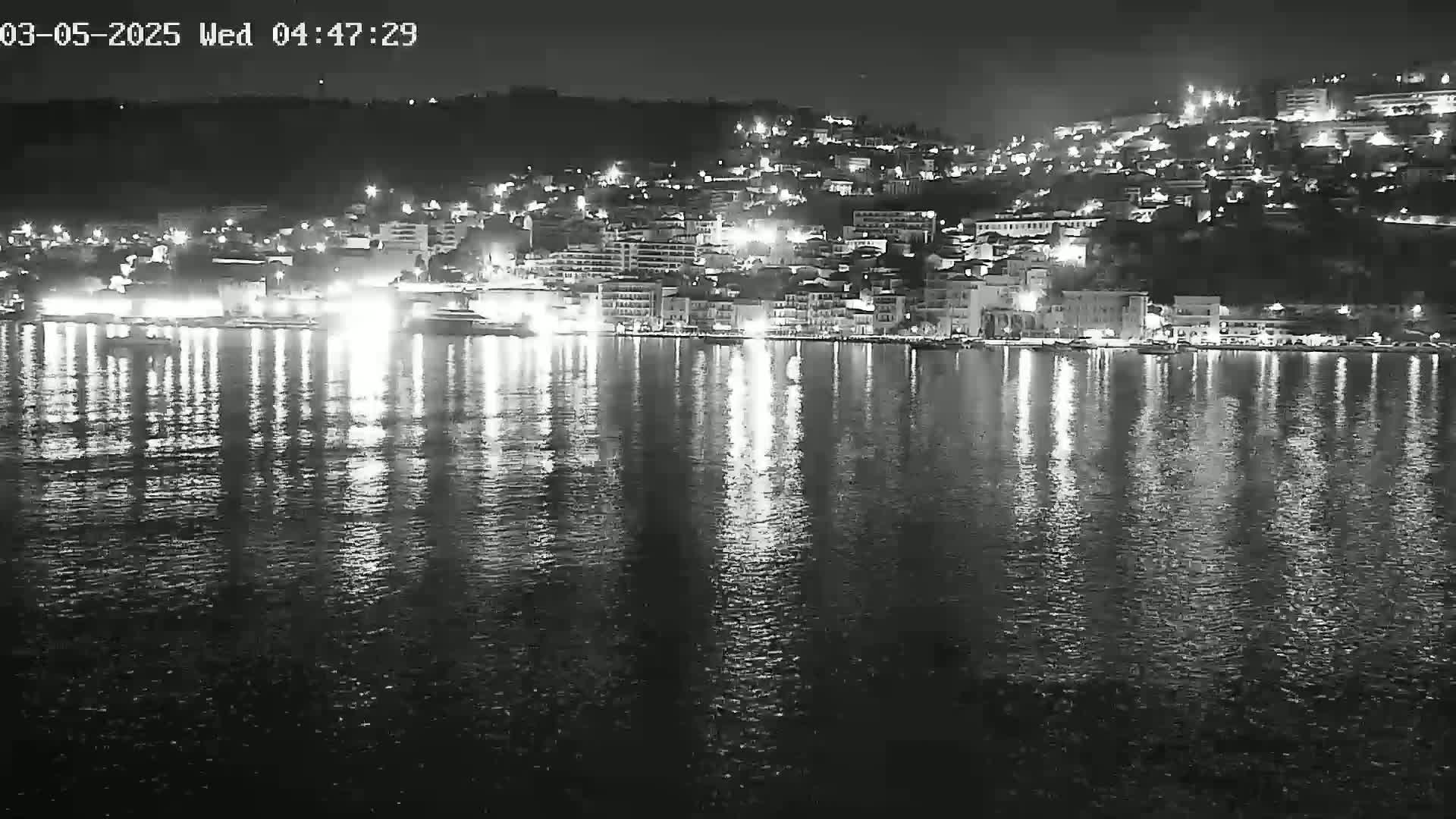 A nighttime view of a city's waterfront, illuminated by lights reflecting on calm water.