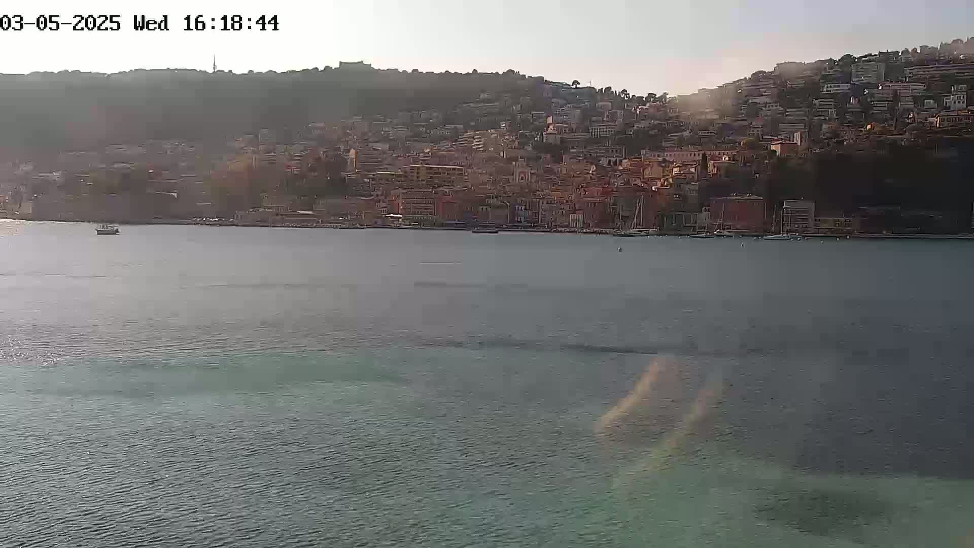 A calm body of water separates the viewer from a hillside town under a hazy sky.