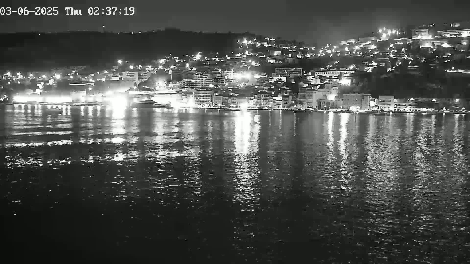 A nighttime view of a city's waterfront, illuminated by lights reflected on calm water.