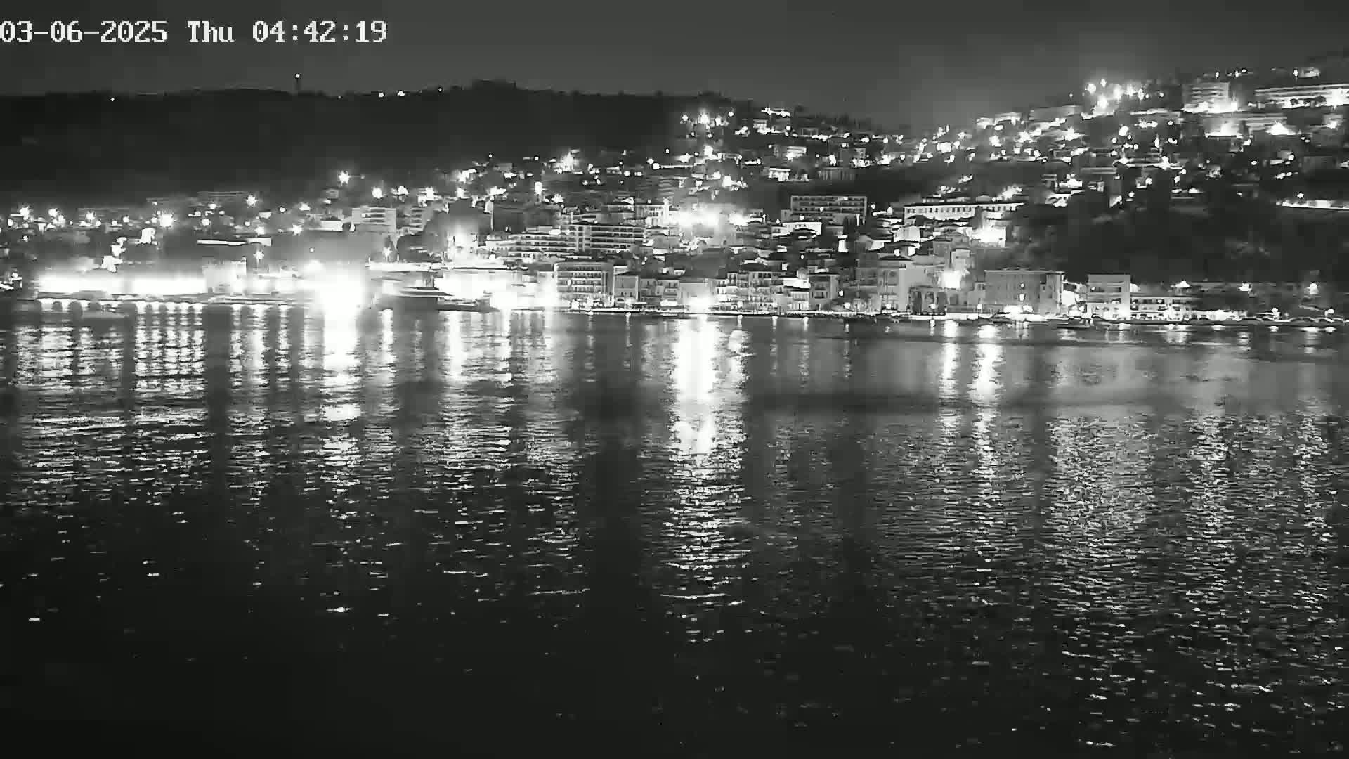 A nighttime view of a city's waterfront, illuminated by lights reflected on calm water.