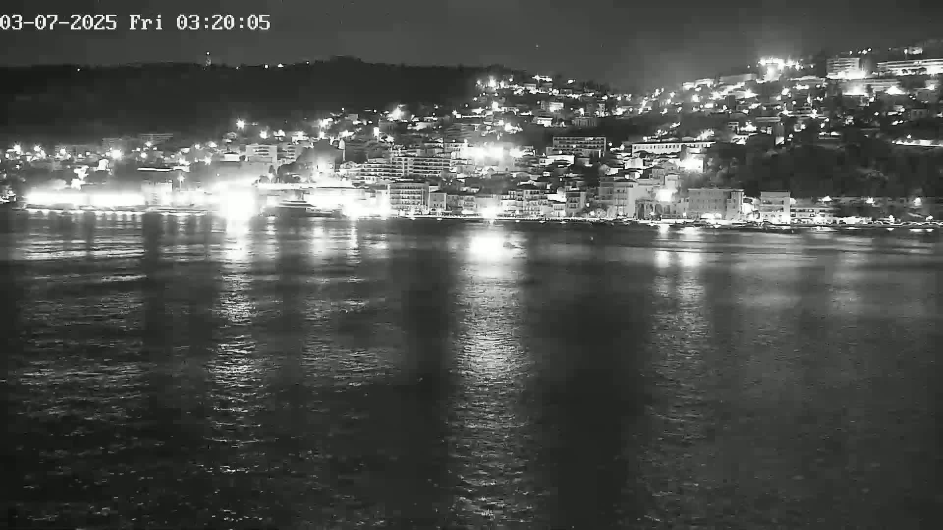 A nighttime view of a city illuminated by lights along a calm body of water.