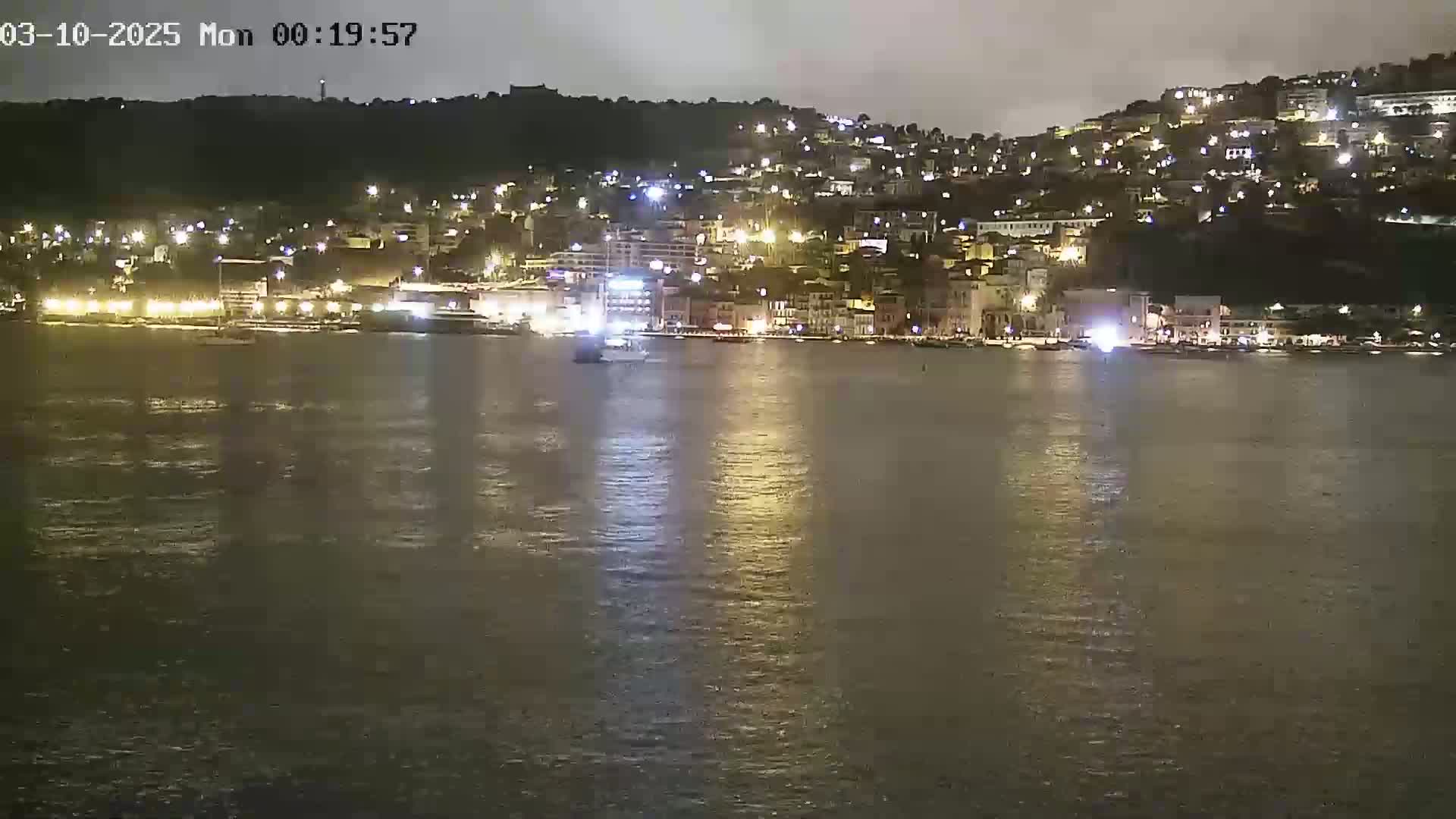 A nighttime view of a city's waterfront, illuminated with lights, reflecting on a calm body of water.