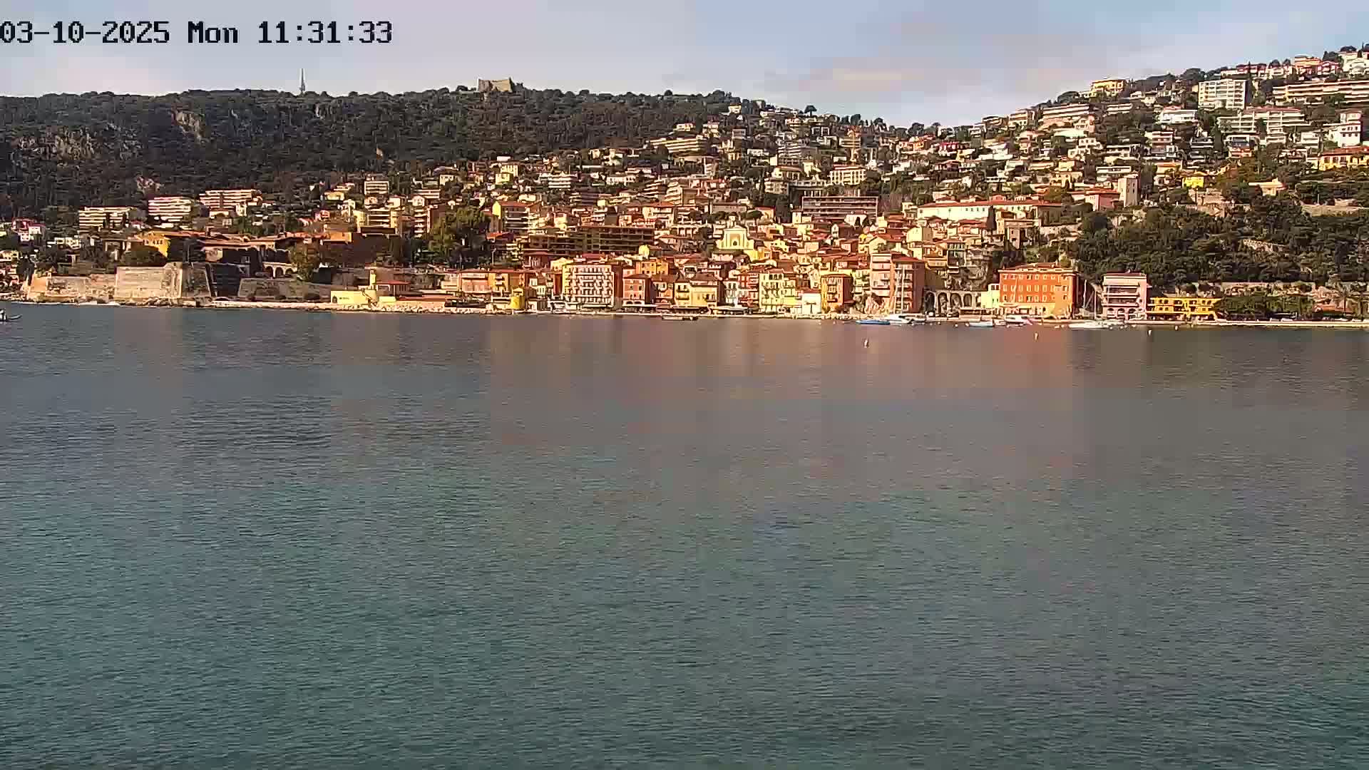 A calm body of water reflects a hillside town of closely packed colorful buildings under a clear sky.