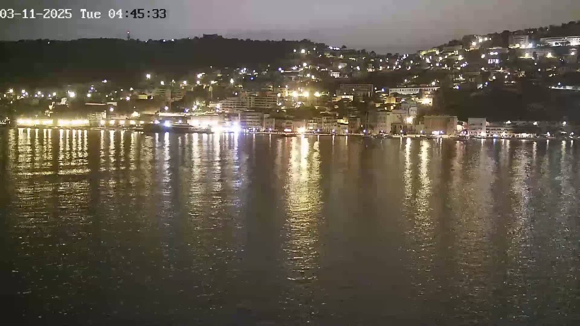 A nighttime view of a city's waterfront, illuminated by lights reflecting on calm water.