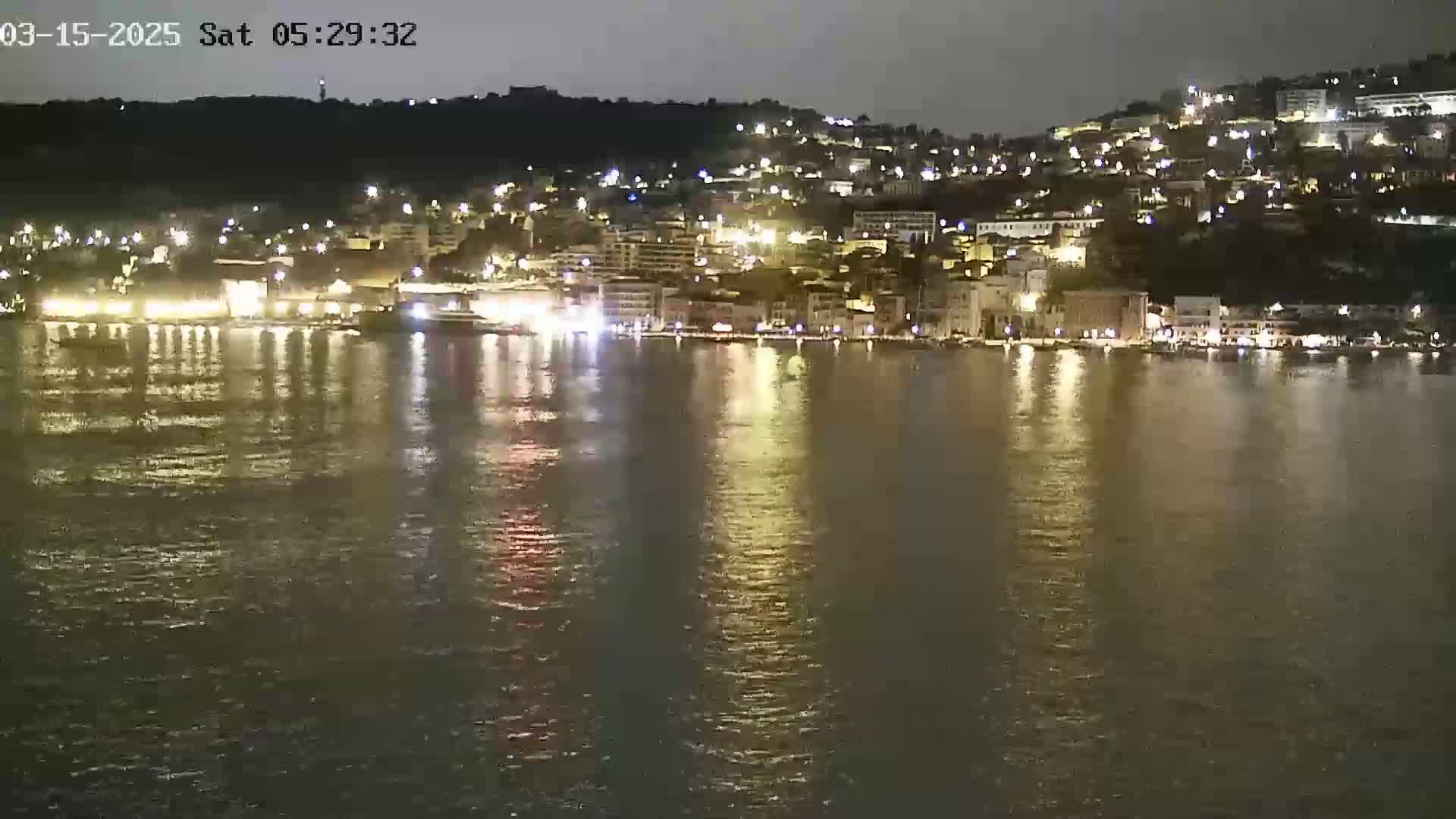 A nighttime view of a city's waterfront, illuminated by lights reflecting on calm water.