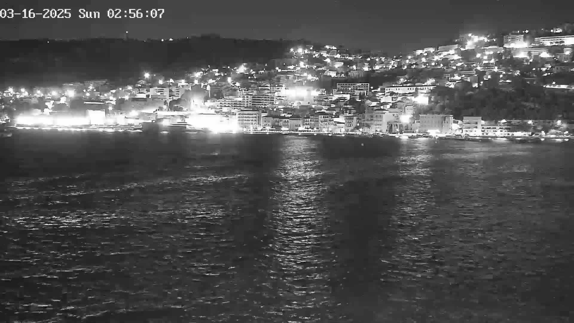 A nighttime, seaside town with many lights is visible across a body of dark water.