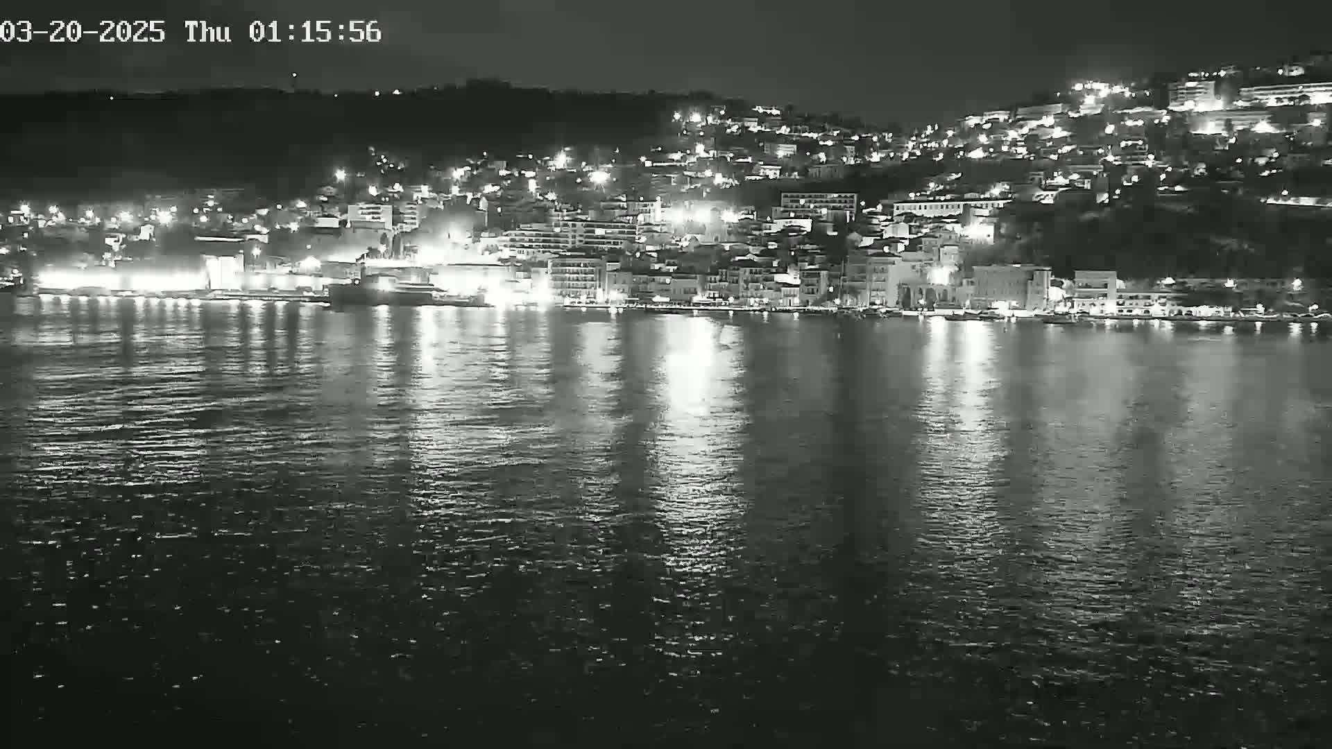 A nighttime view of a town's waterfront, illuminated by lights reflecting on calm water.