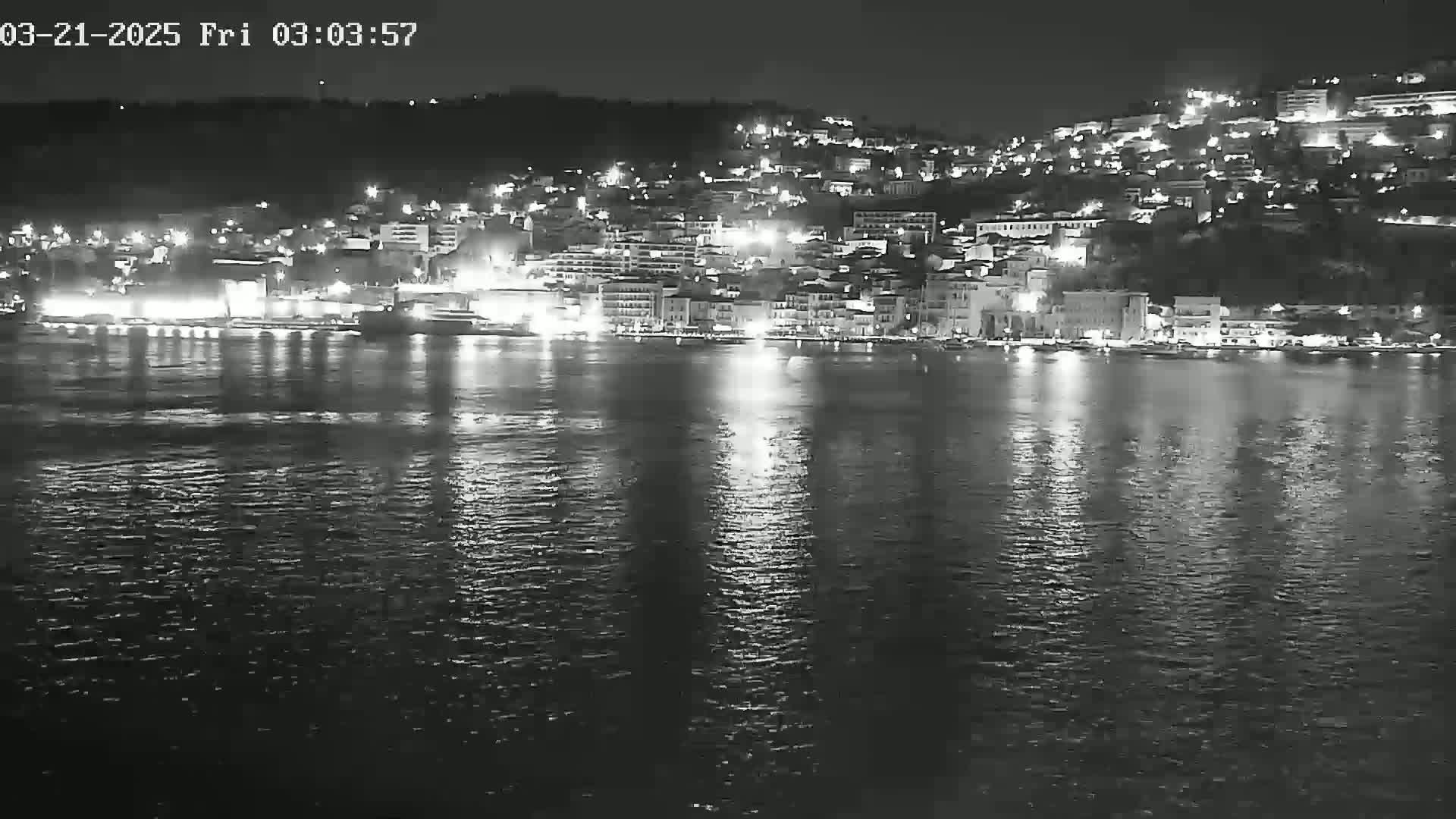 A nighttime view of a city's waterfront, illuminated by lights reflecting on calm water.