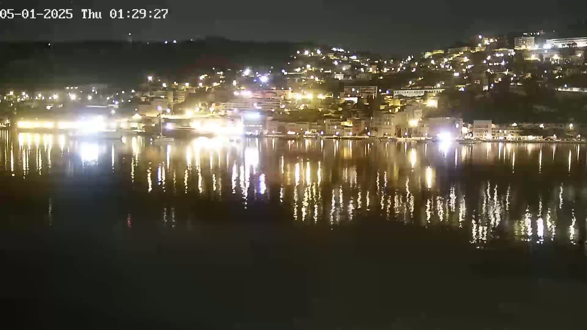 A nighttime view of a city's waterfront, illuminated with many lights reflected on the calm water.