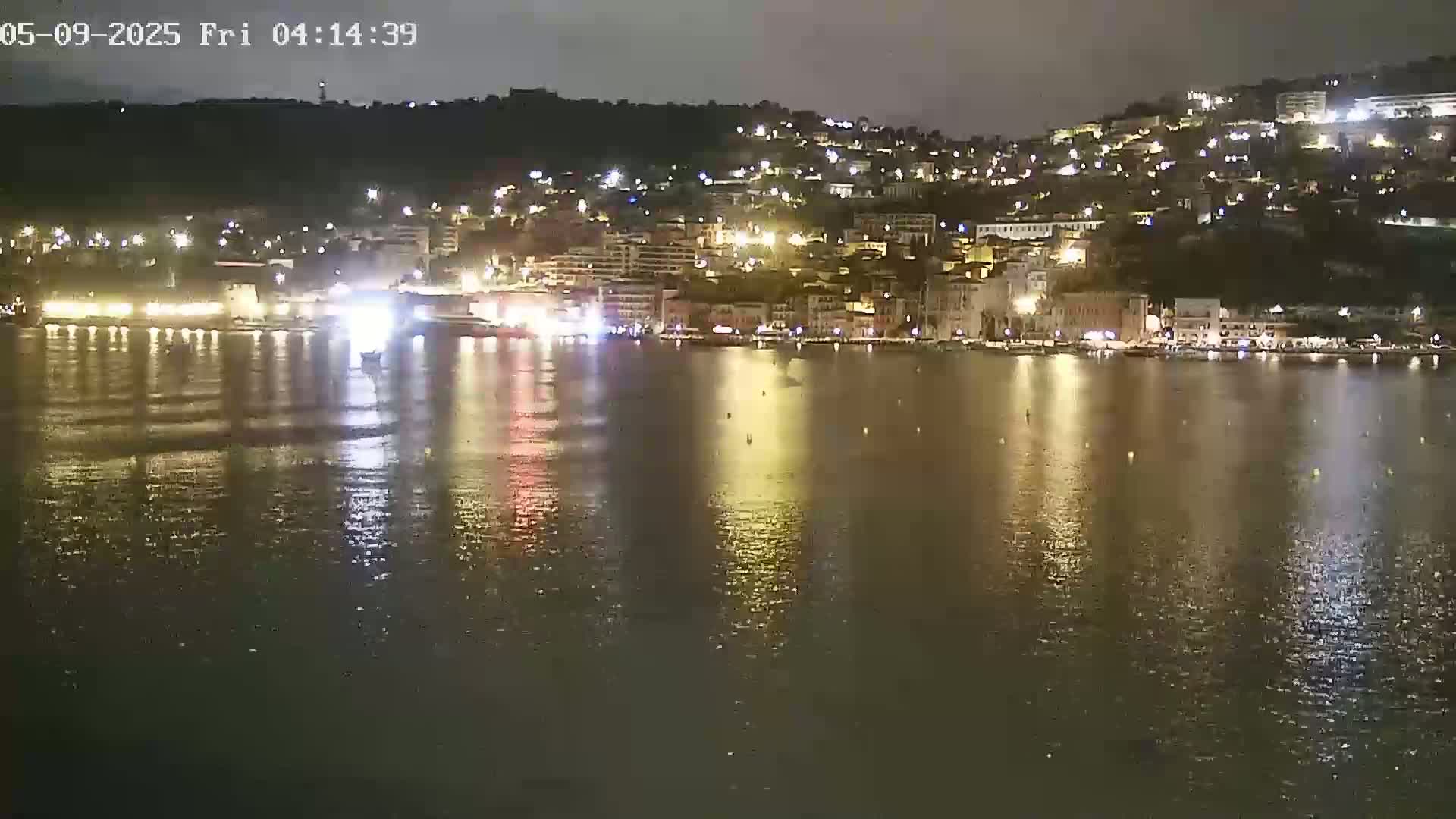 A nighttime view of a town's waterfront, illuminated by lights reflecting on calm water.