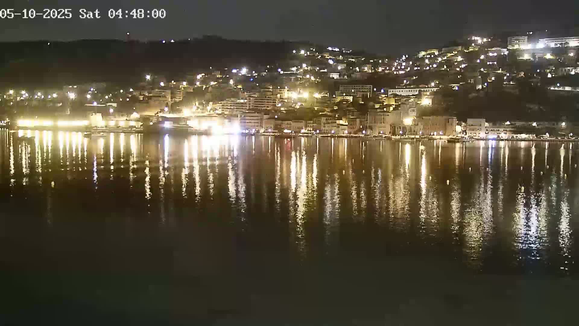 A brightly lit waterfront town at night is reflected in a calm body of water.