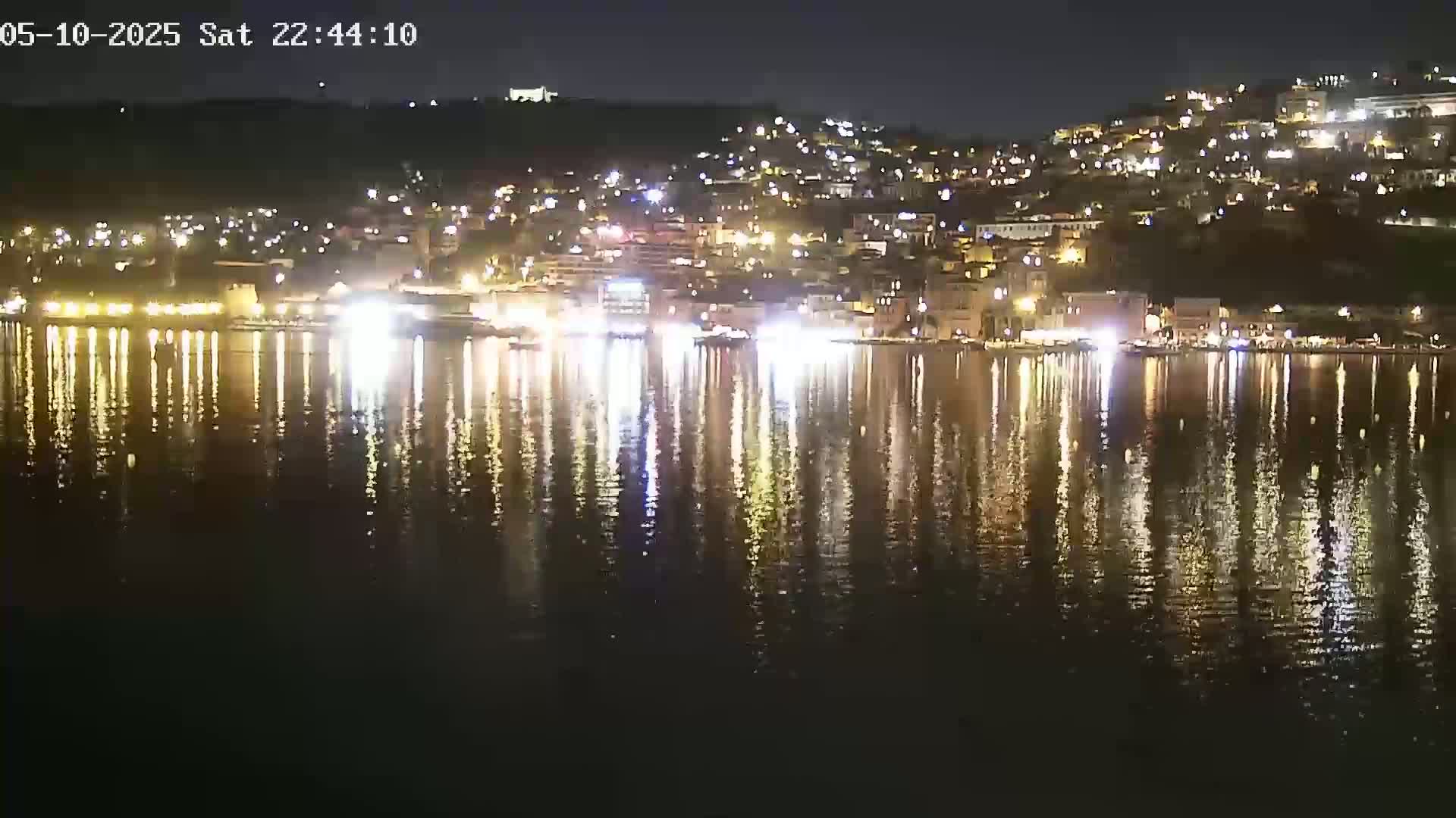 The lights of a town at night are reflected in a calm body of water.
