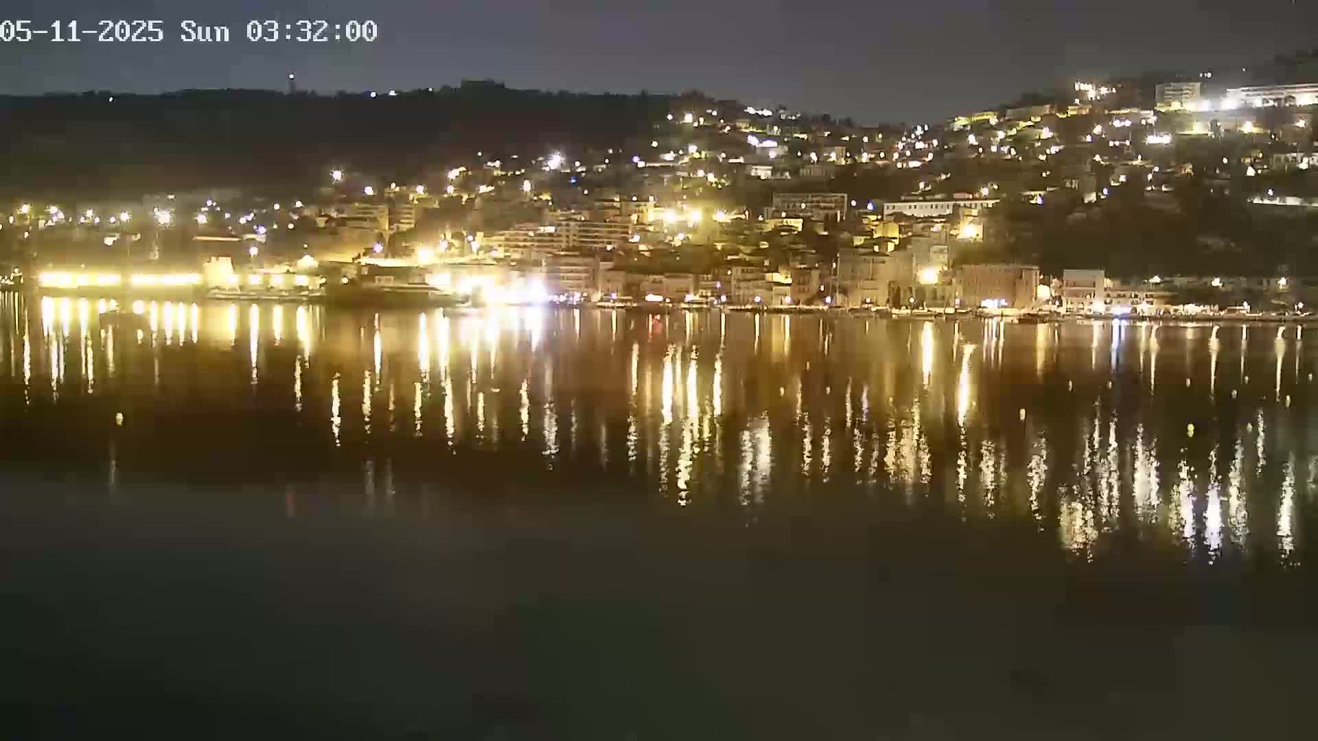A nighttime view of a city's waterfront, illuminated by many lights reflected on a calm body of water.