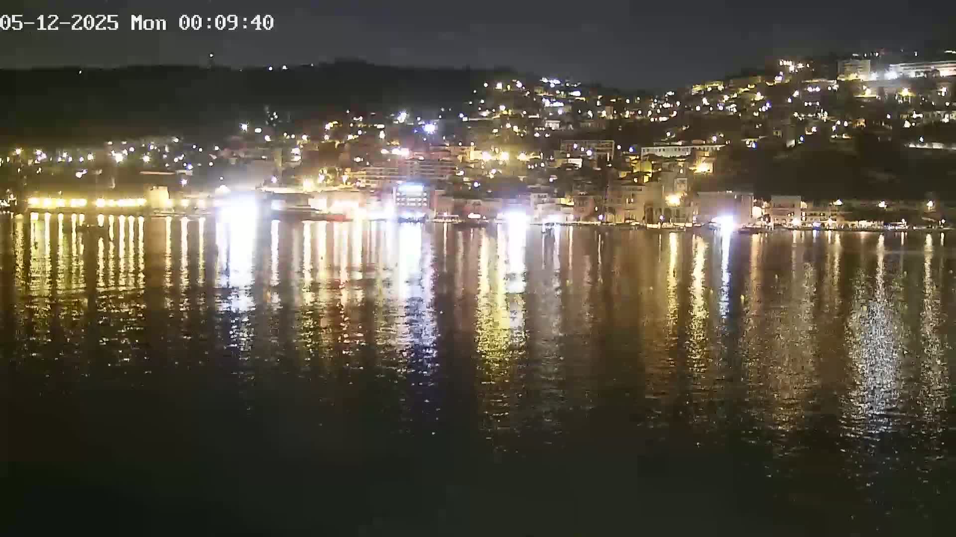 A nighttime view of a town's waterfront, illuminated by lights reflecting on calm water.