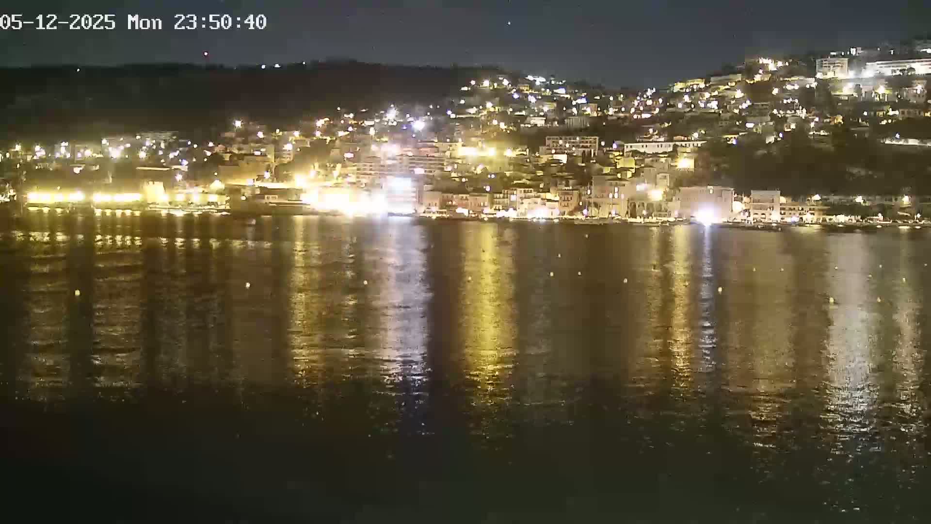 A nighttime view of a brightly lit waterfront town on a calm sea under a clear, dark sky.