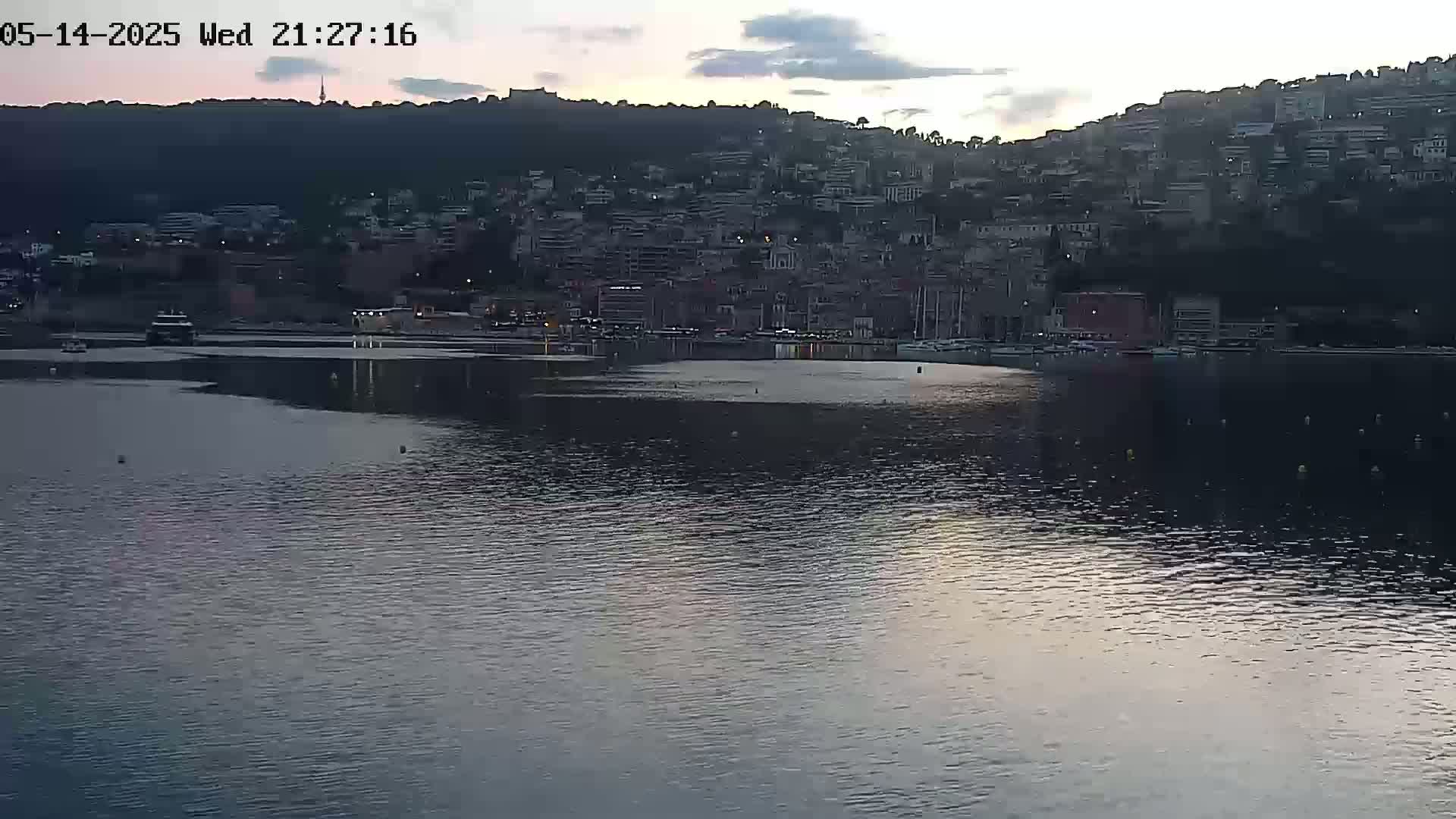 A calm body of water reflects the twilight sky and a hillside town at dusk.