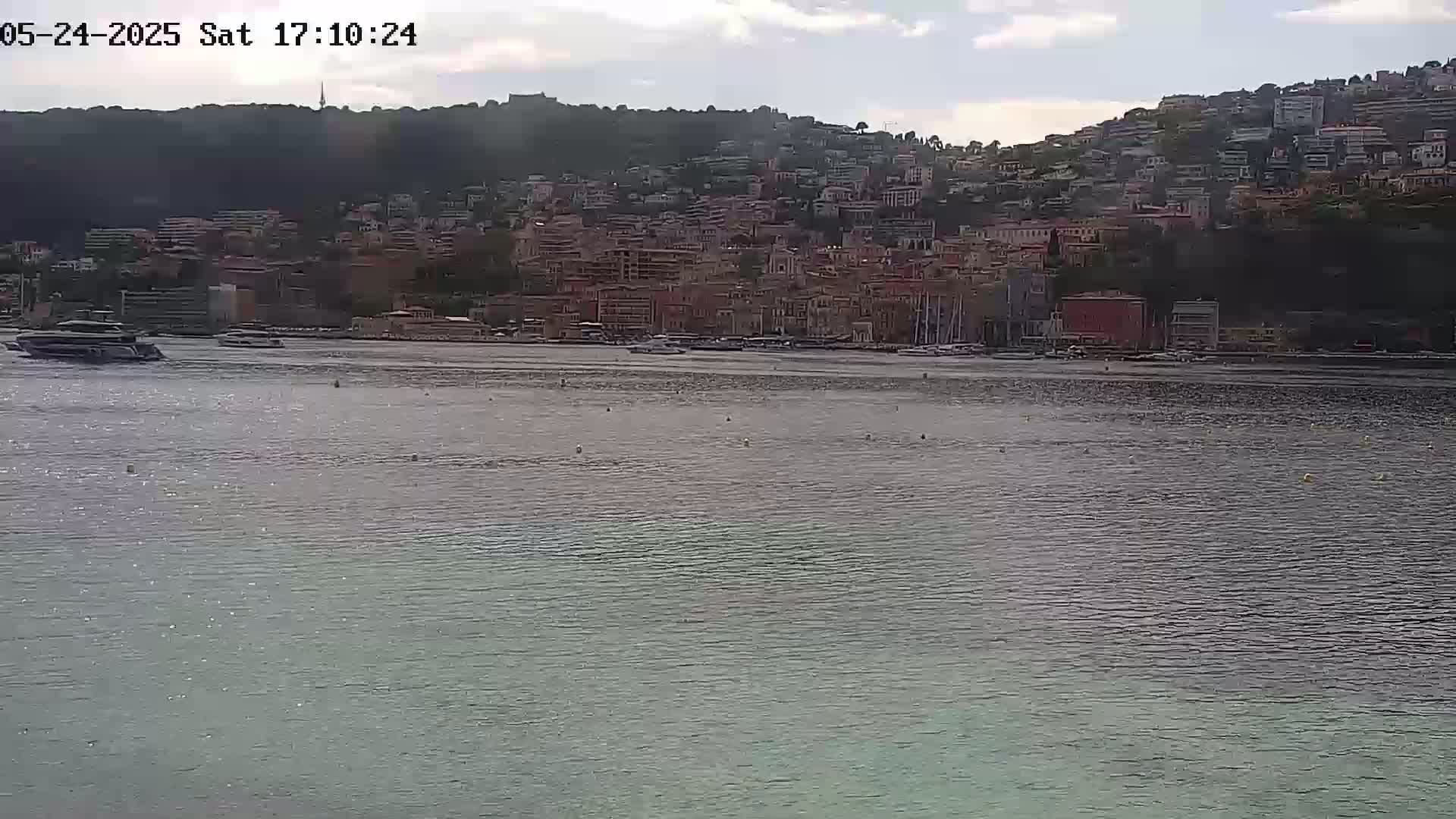 A calm body of water sits in front of a hillside town under a partly cloudy sky.