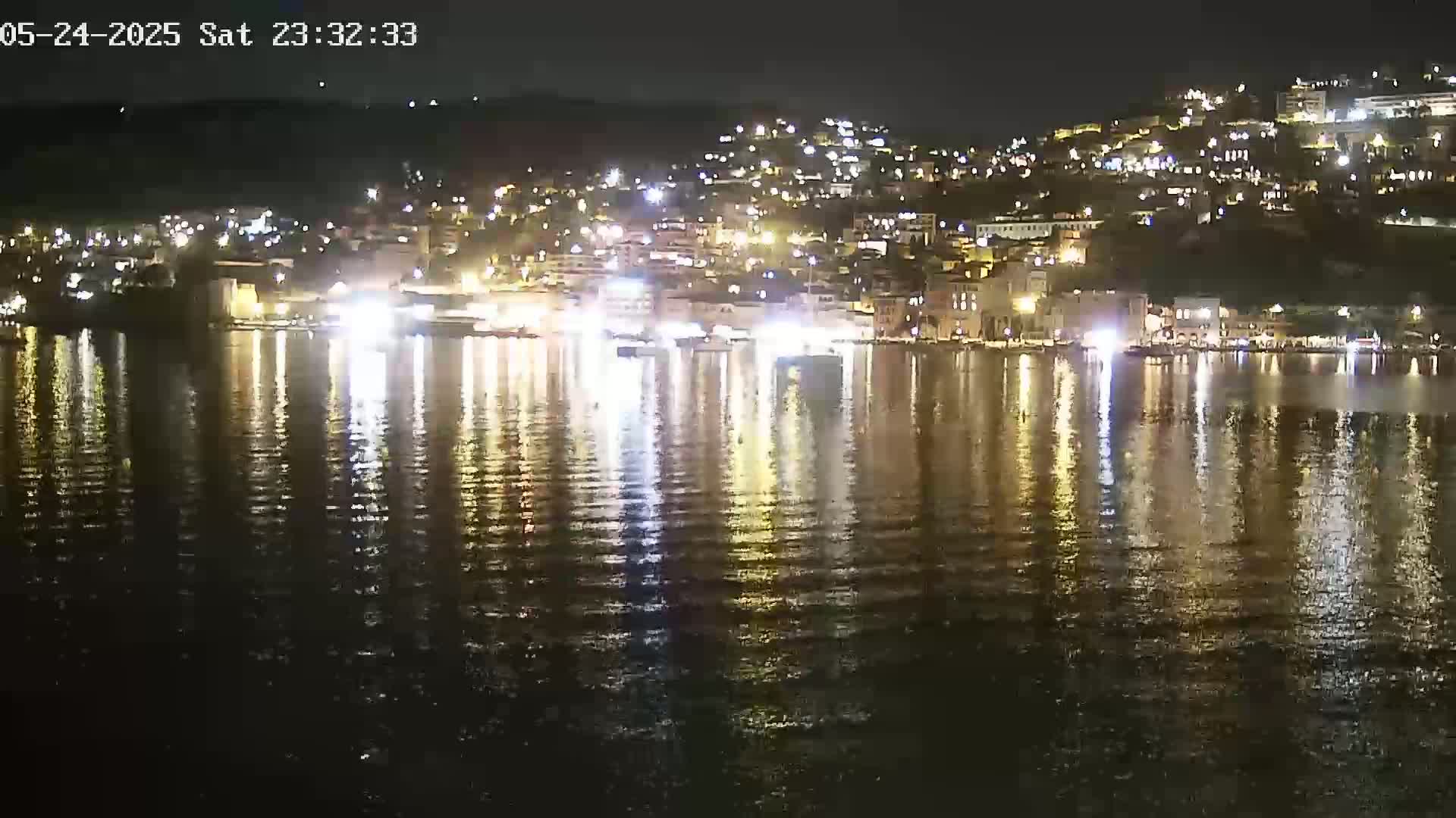 A brightly lit waterfront town at night is reflected in calm water.
