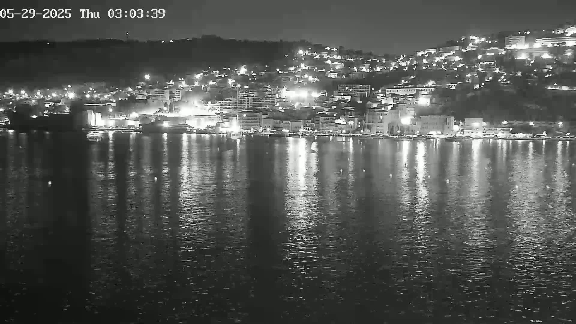 A nighttime view of a city's waterfront, illuminated by lights reflecting on calm water.