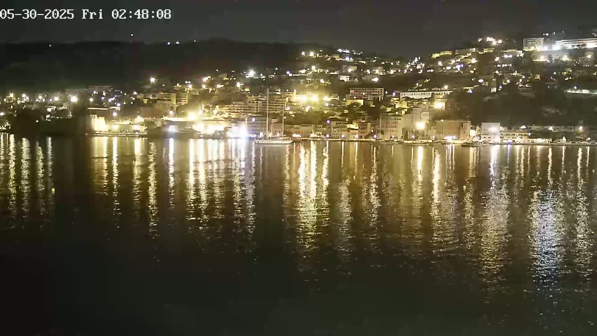 A nighttime view of a town's waterfront, illuminated by many lights reflecting on calm water.