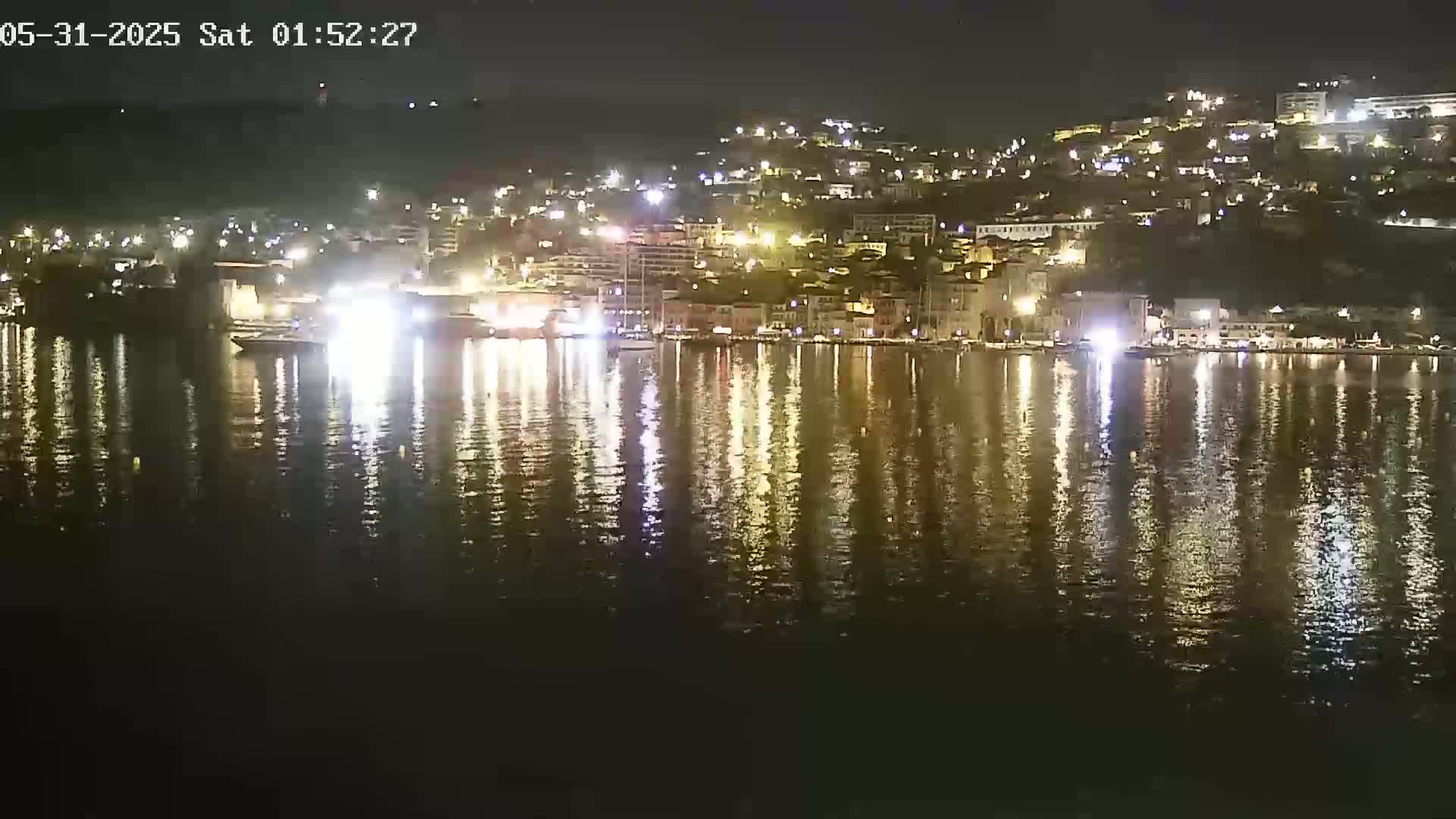 A nighttime view of a waterfront town with lights reflecting on calm water.