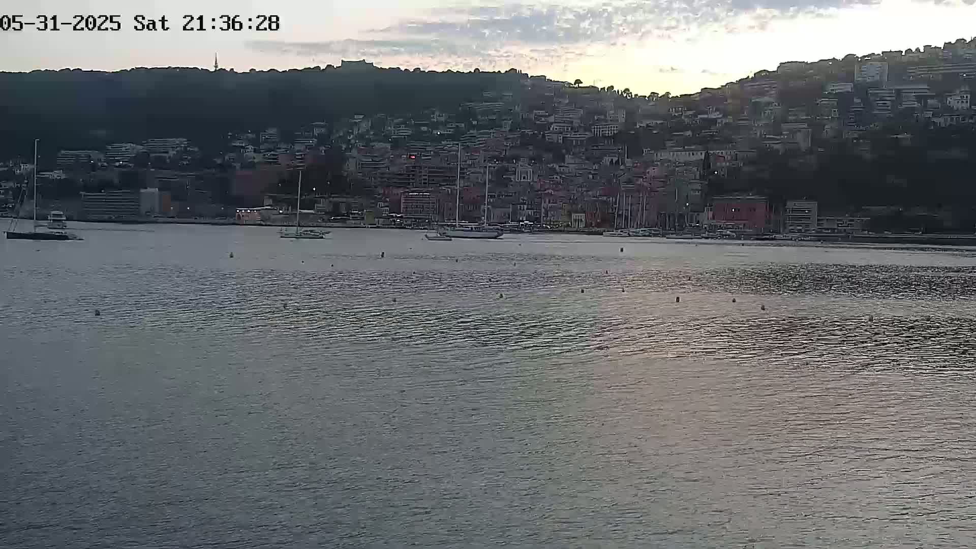 A calm body of water sits in front of a hillside town under a twilight sky.