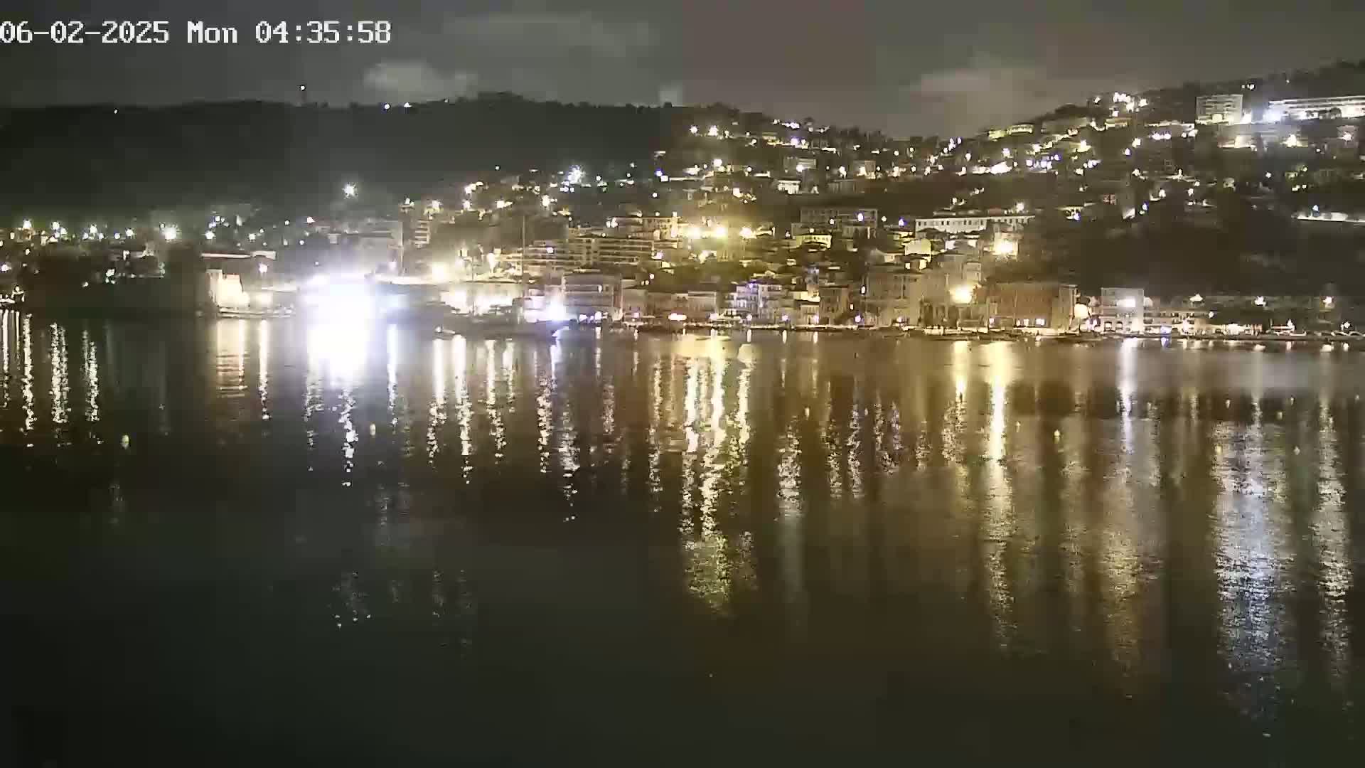 A nighttime view of a waterfront town with many lights reflected on calm water.