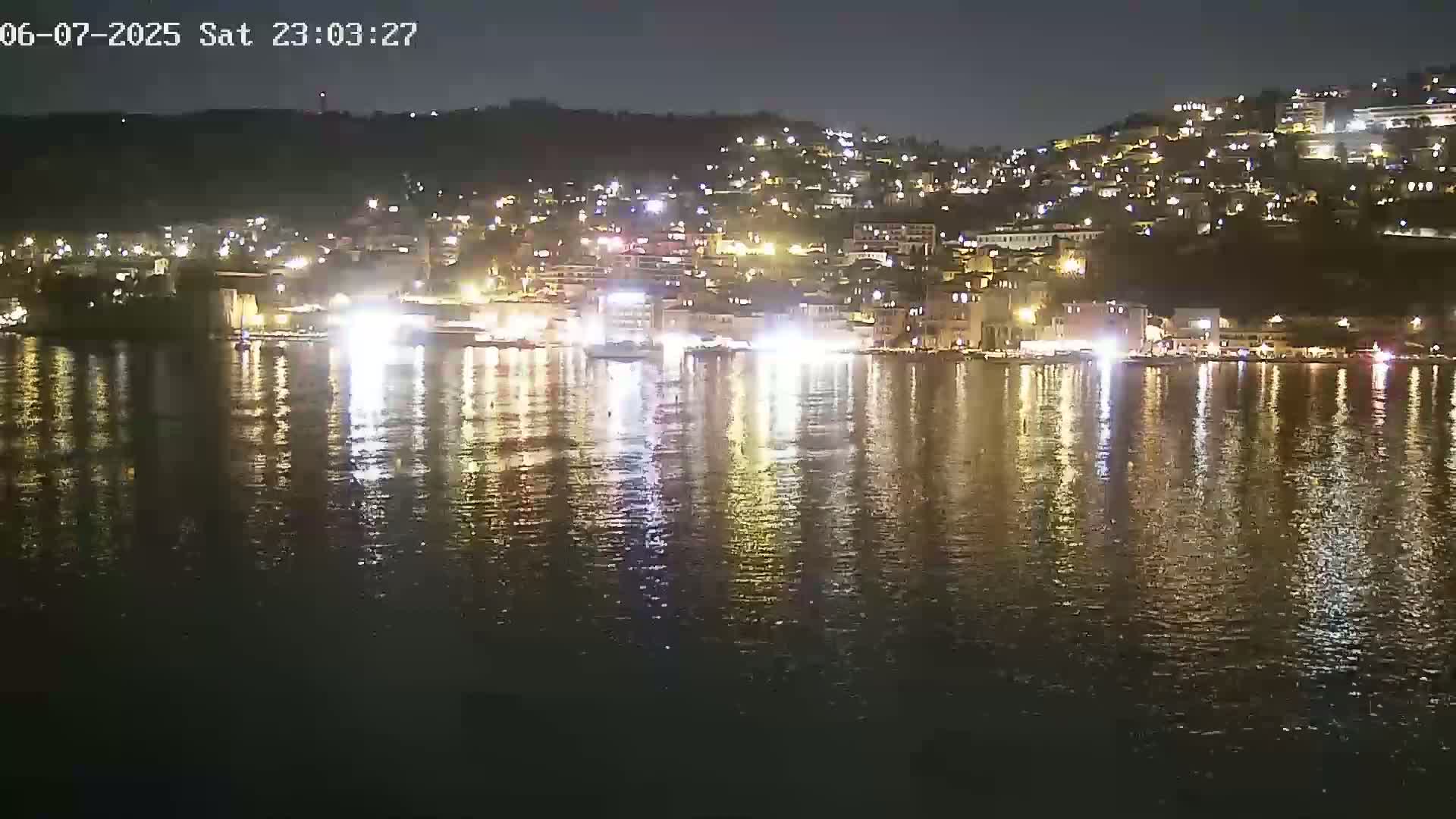 A night-time view of a town's lights reflected on calm water.