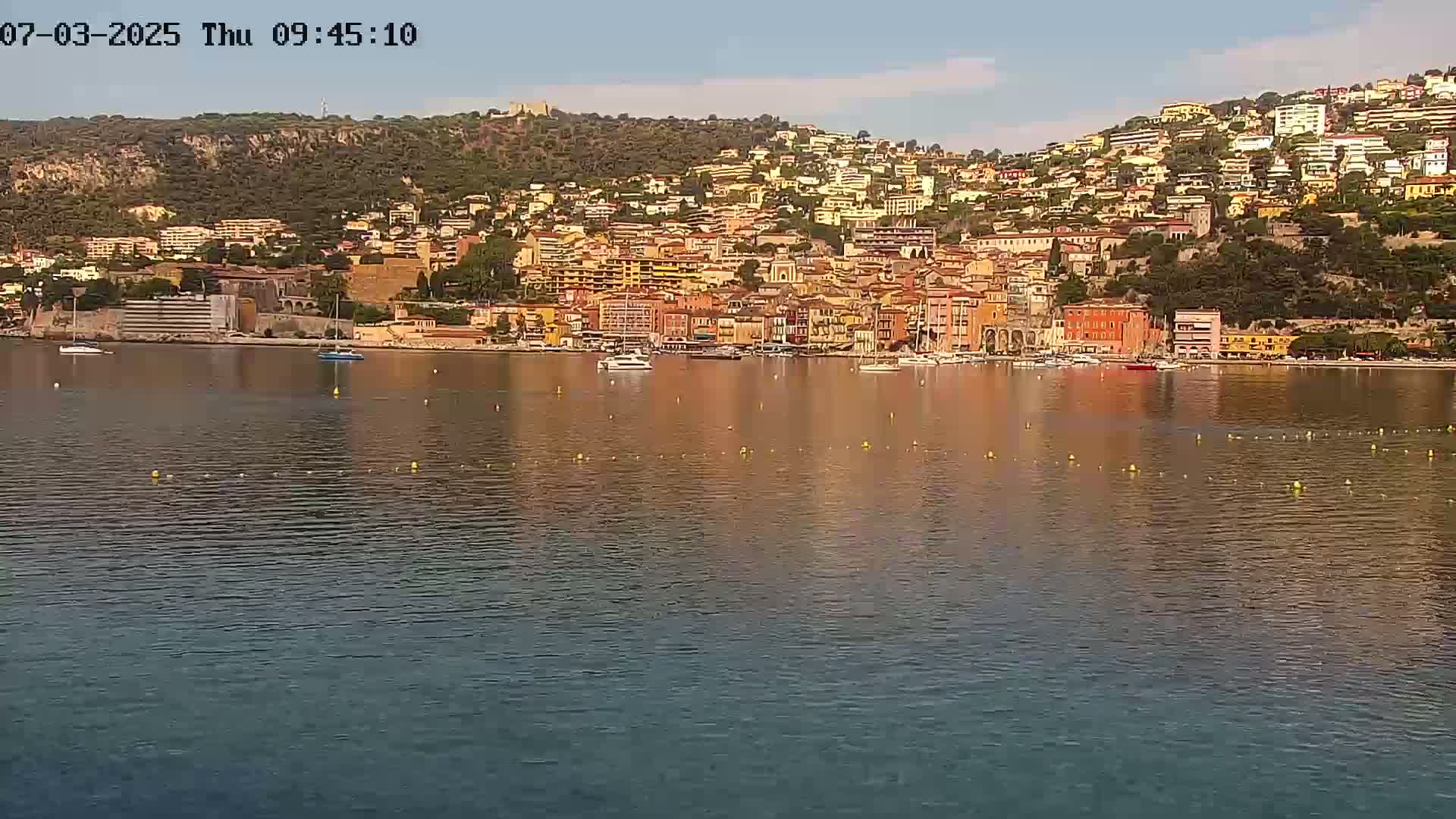 A hillside town with colorful buildings sits beside a calm body of water on a sunny day.