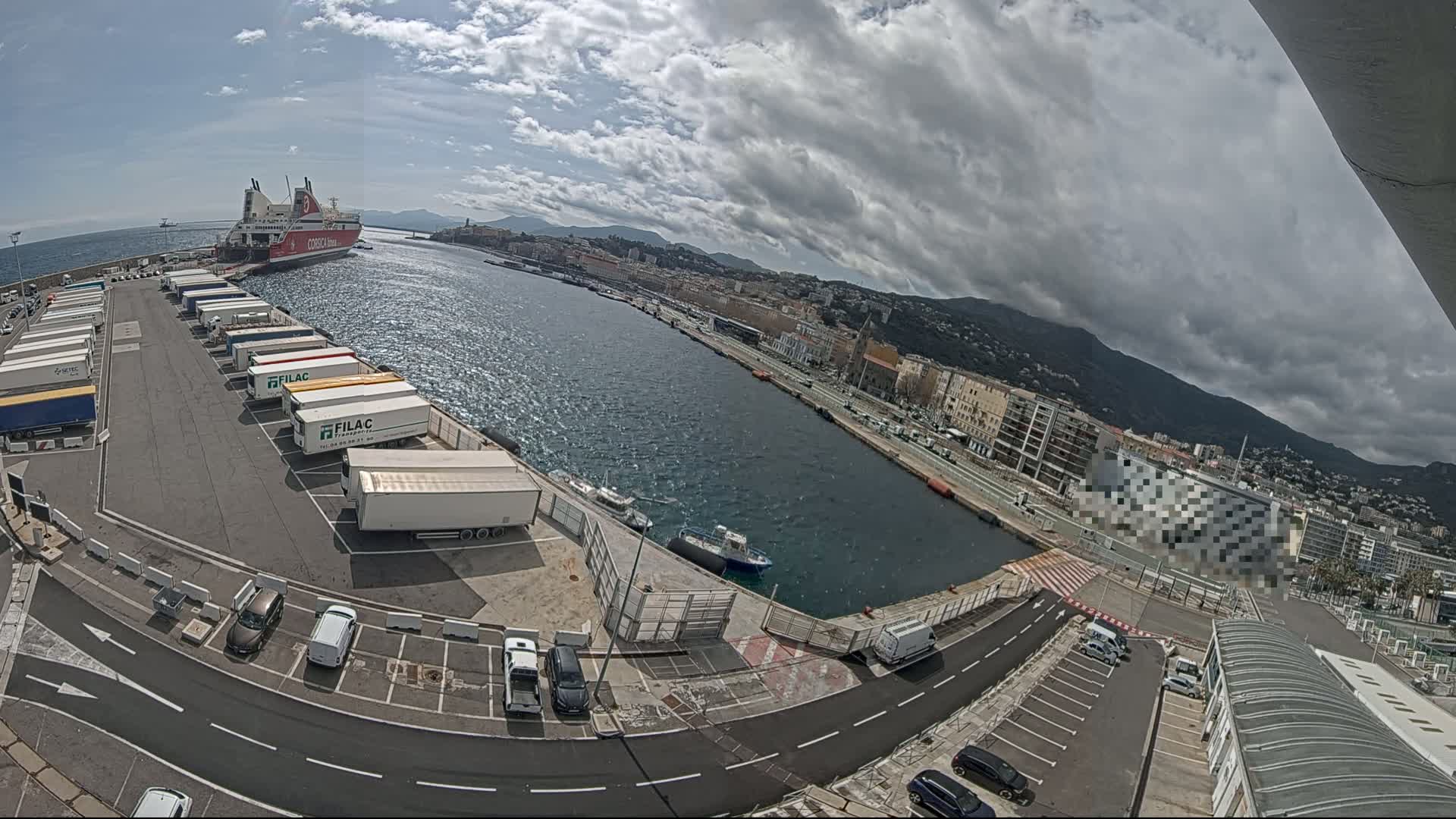A large ferry is docked at a harbor next to a city under a partly cloudy sky.