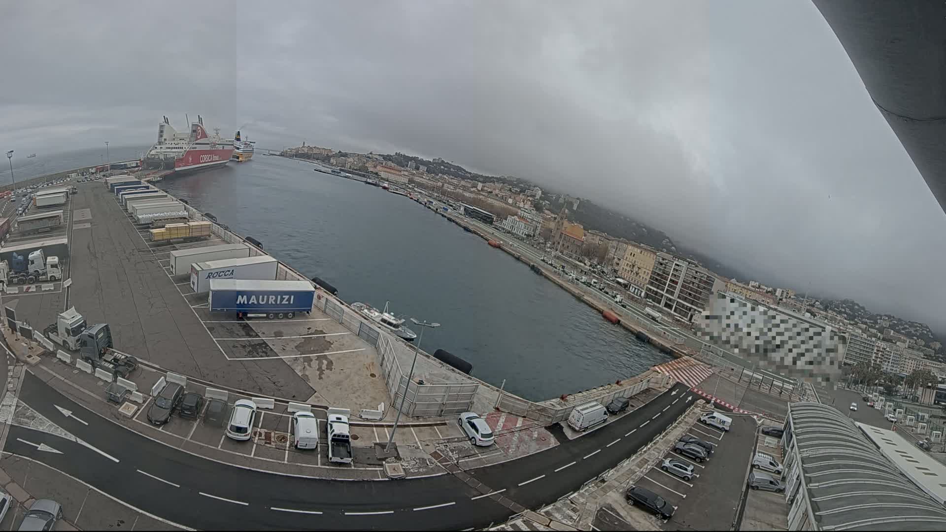 A ferry is docked at a harbor on an overcast day, with numerous trucks and cars parked in the surrounding area.