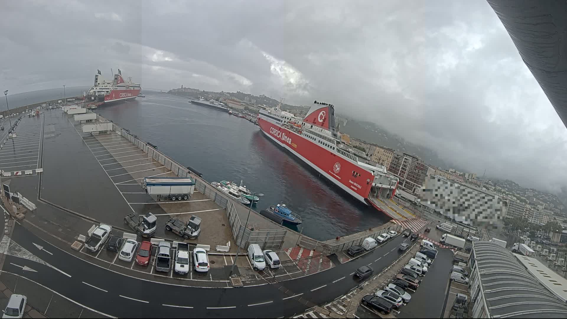 Two large ferries are docked at a port on an overcast day, with numerous cars parked in a lot nearby.