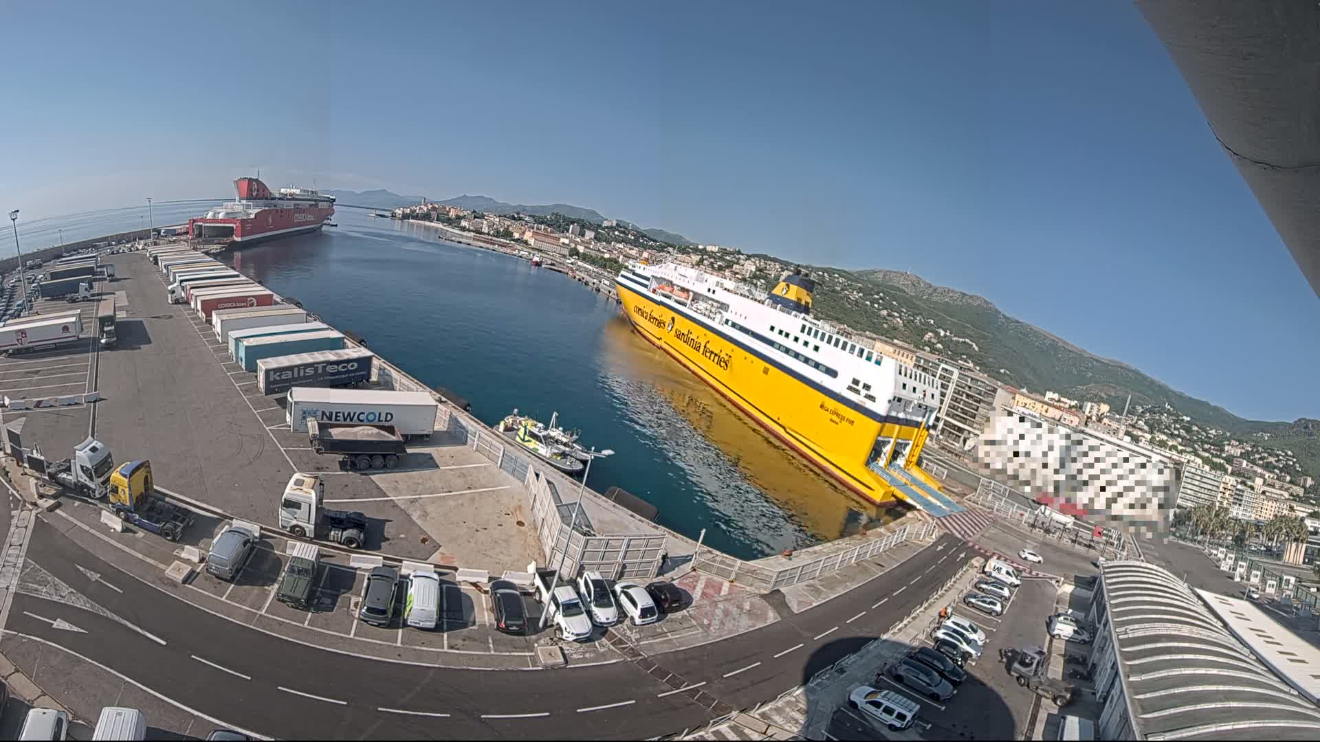 A yellow and a red ferry are docked at a port on a sunny day, with numerous cars and trucks parked nearby.