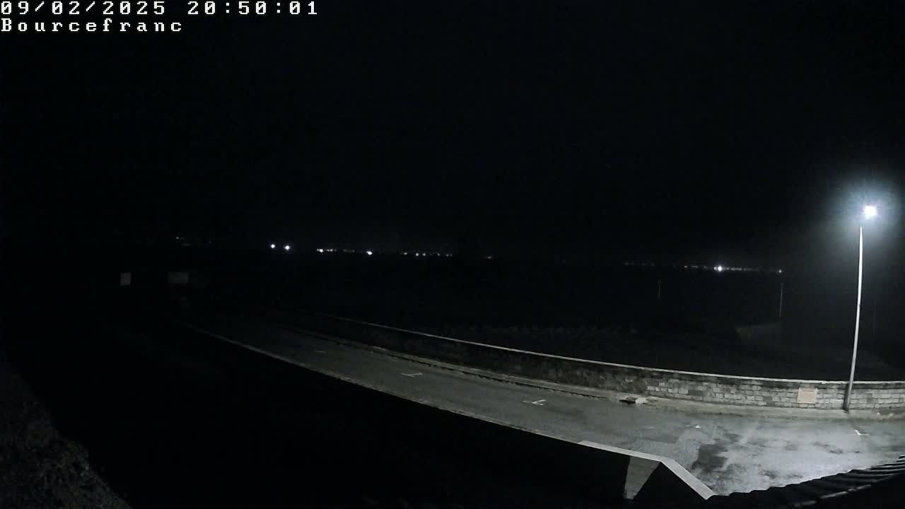 A nighttime view shows a dark, empty road next to a low wall, illuminated by a single streetlight in the distance.