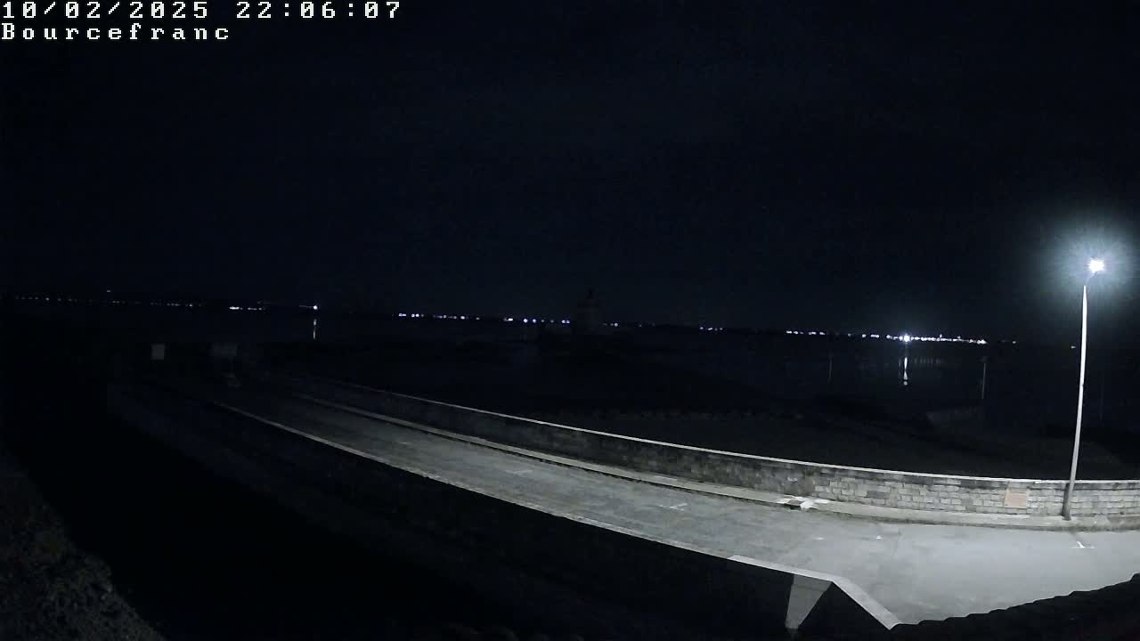 A nighttime view of a paved area leading to a body of water under a dark, clear sky, illuminated by a single lamppost.