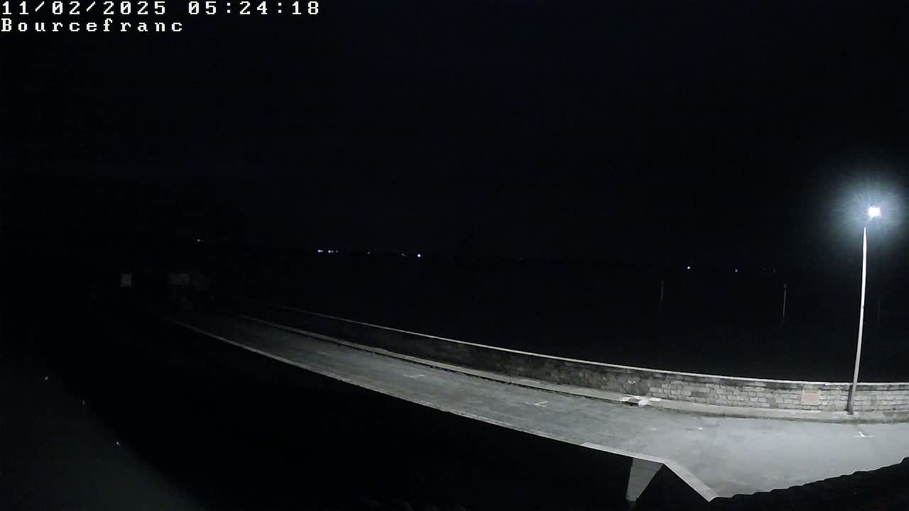 A nighttime view of a low-lit road and wall extending into the darkness, illuminated by a single lamppost.