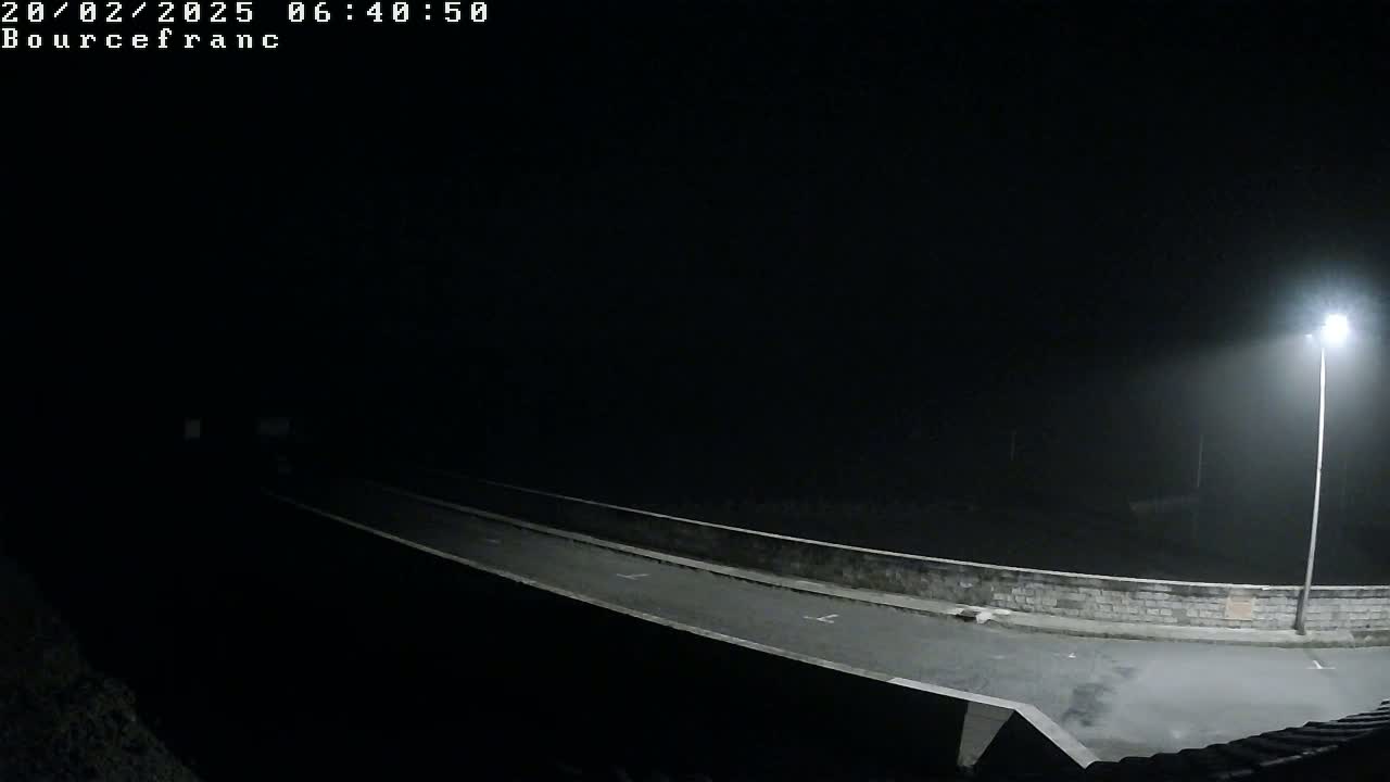 A nighttime, foggy scene shows a two-lane road on a bridge illuminated by a single streetlight.