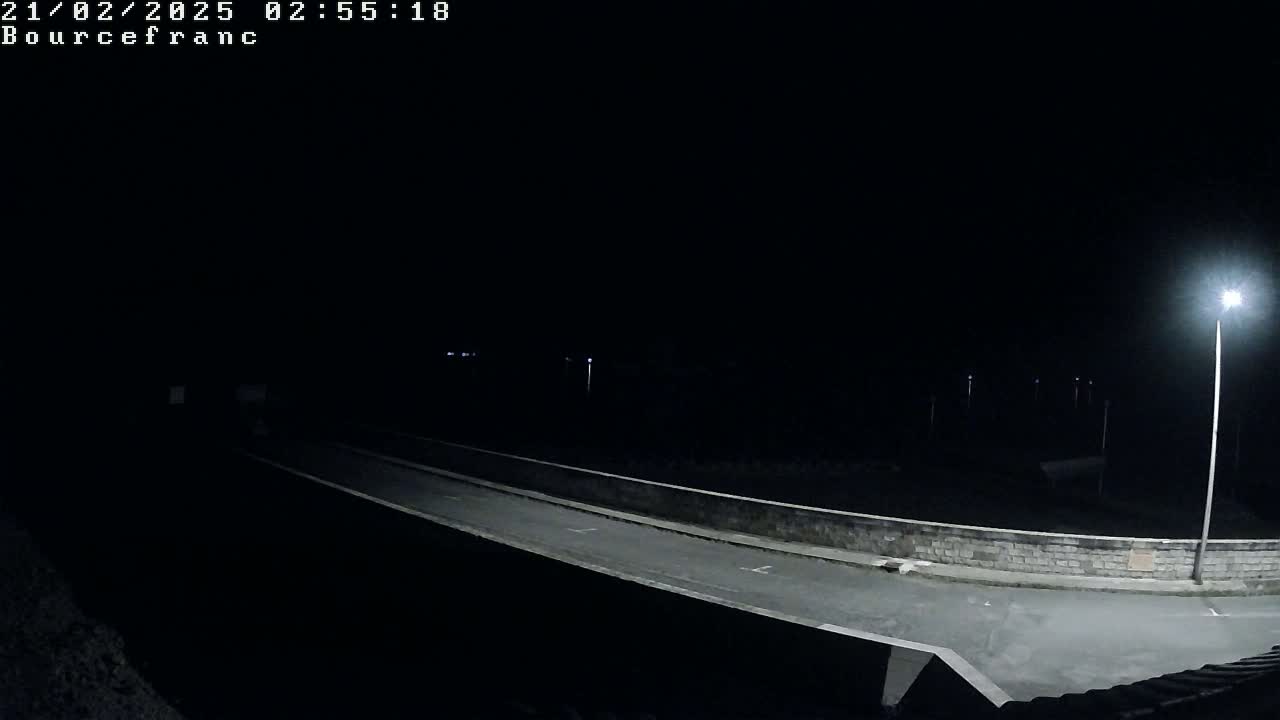 A nighttime view of a dark, empty road lit by several streetlights, with a low stone wall on either side.
