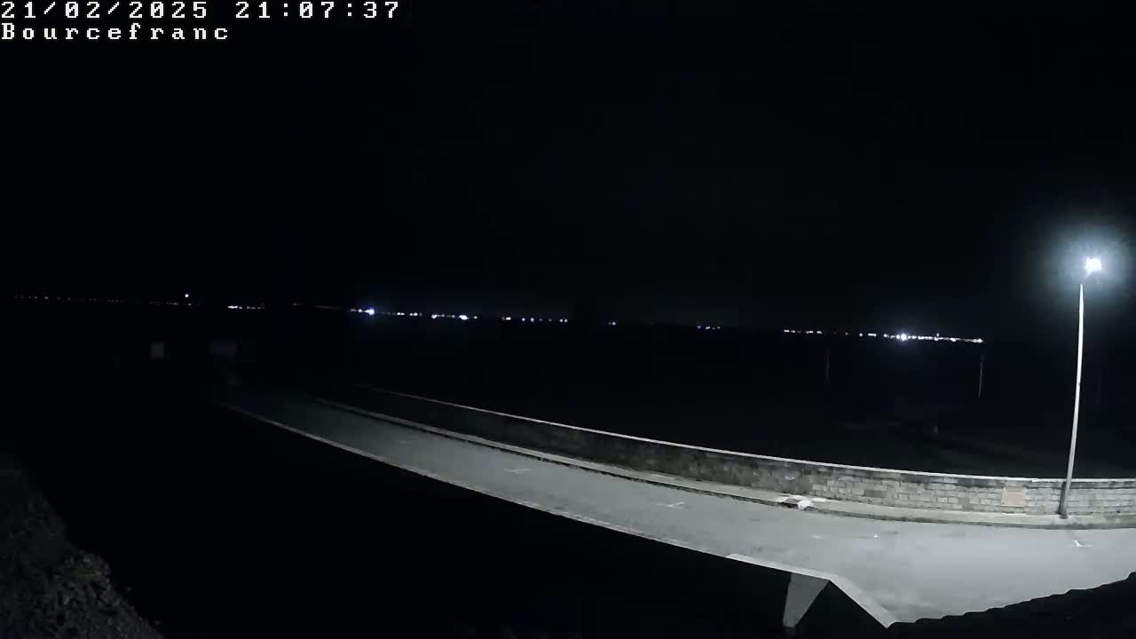 A nighttime view of a roadway on a bridge, with a low light level and distant city lights visible in the background.