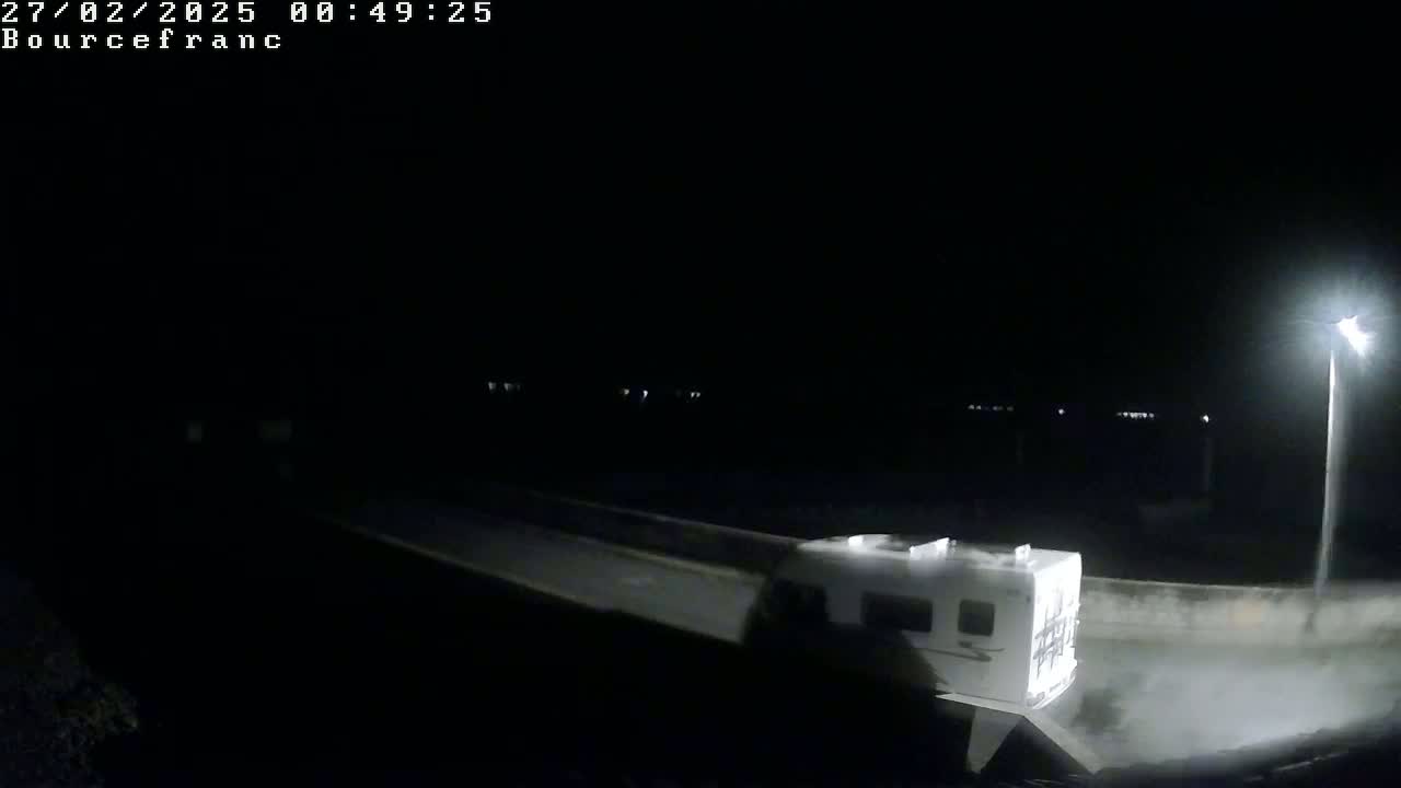A white camper van is parked at night under a single streetlight.