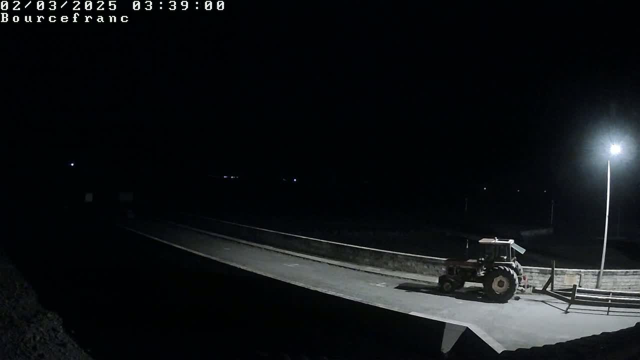 A tractor with a trailer is parked on a dark road at night, illuminated by a single streetlight.