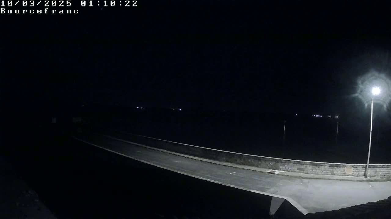 A nighttime view of a dark road extending from a low wall toward a dark body of water under a clear sky.