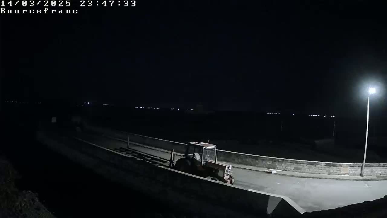 A red tractor is parked on a dark road at night, illuminated by a single streetlight.