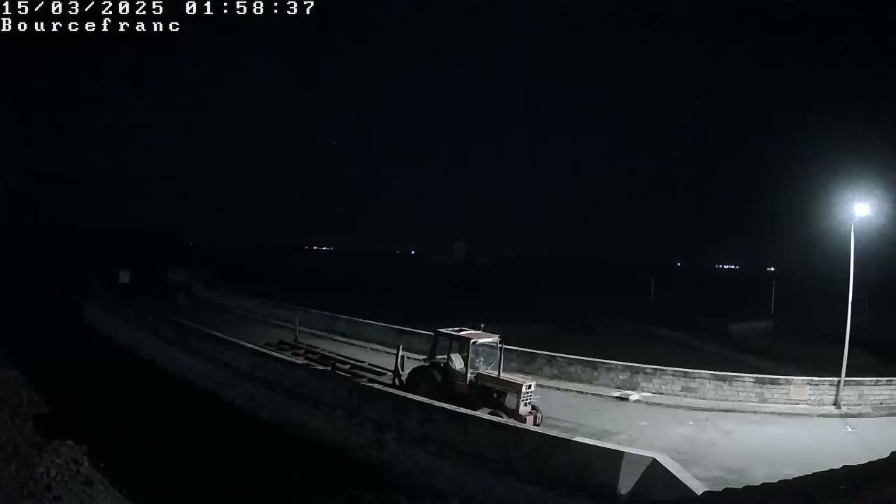 A red tractor is parked on a dark road at night, illuminated by a single streetlight.