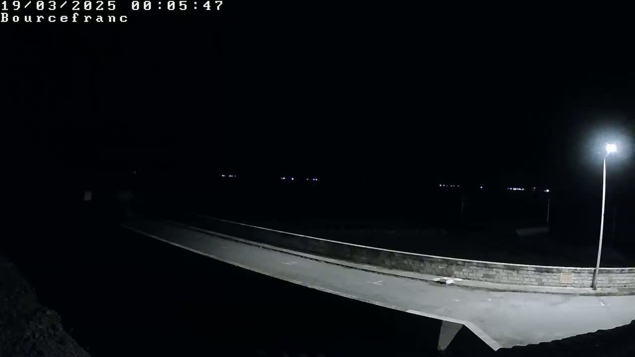 A nighttime, low-angle view shows a roadway curving away from the viewer, illuminated by a single lamppost on the right, and faint lights in the distance.