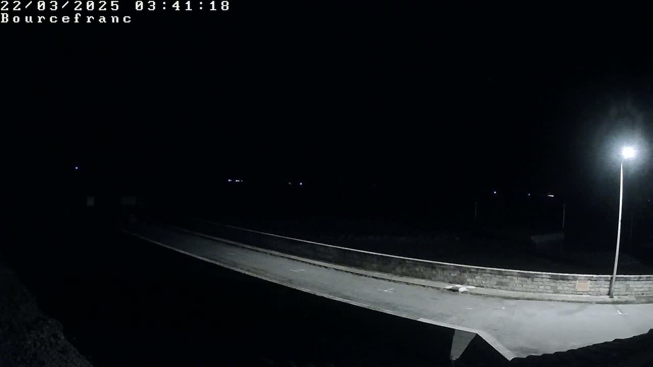 A nighttime, low-angle view shows a dark, empty roadway illuminated by a single lamppost.