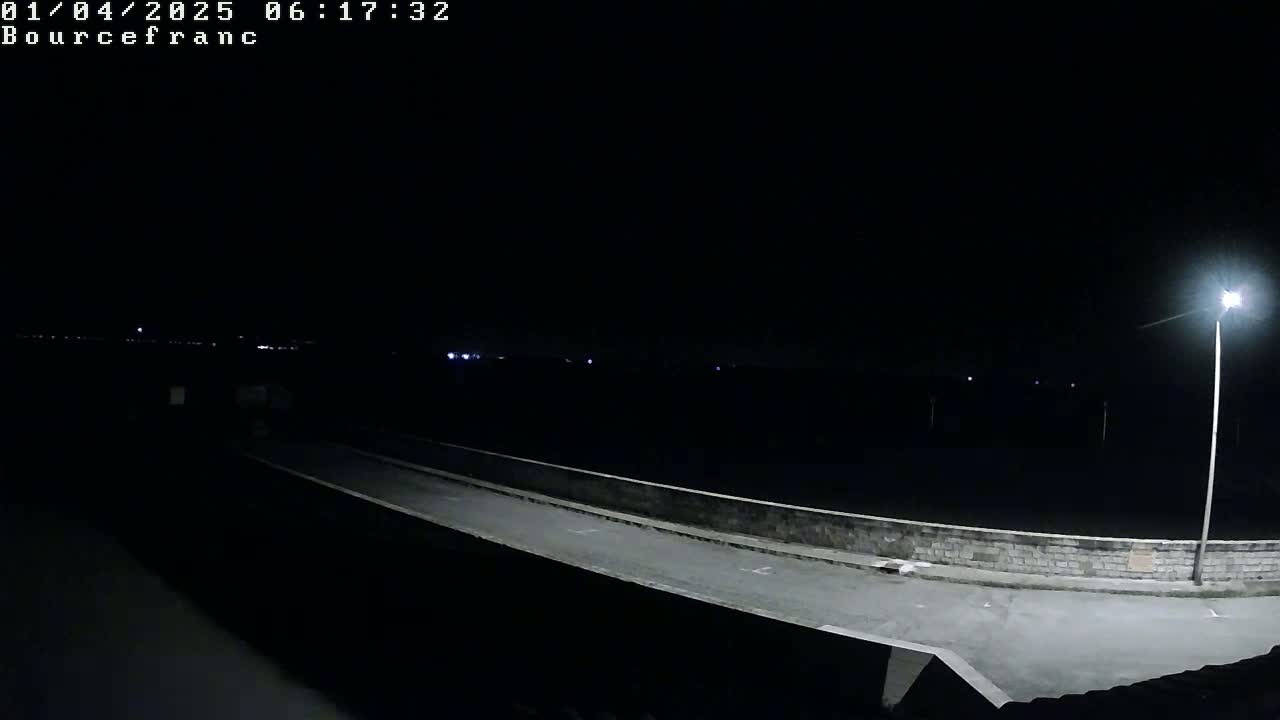 A nighttime view of a paved road on a bridge, illuminated by a single streetlight, with a dark, seemingly empty landscape extending beyond.
